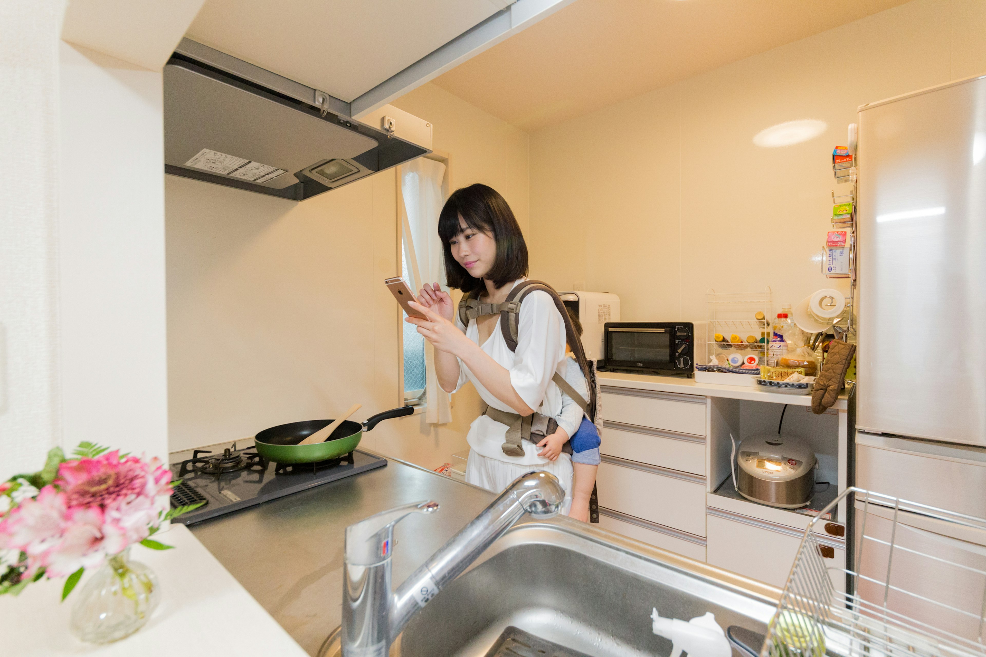 A woman in a bright kitchen using a smartphone while cooking