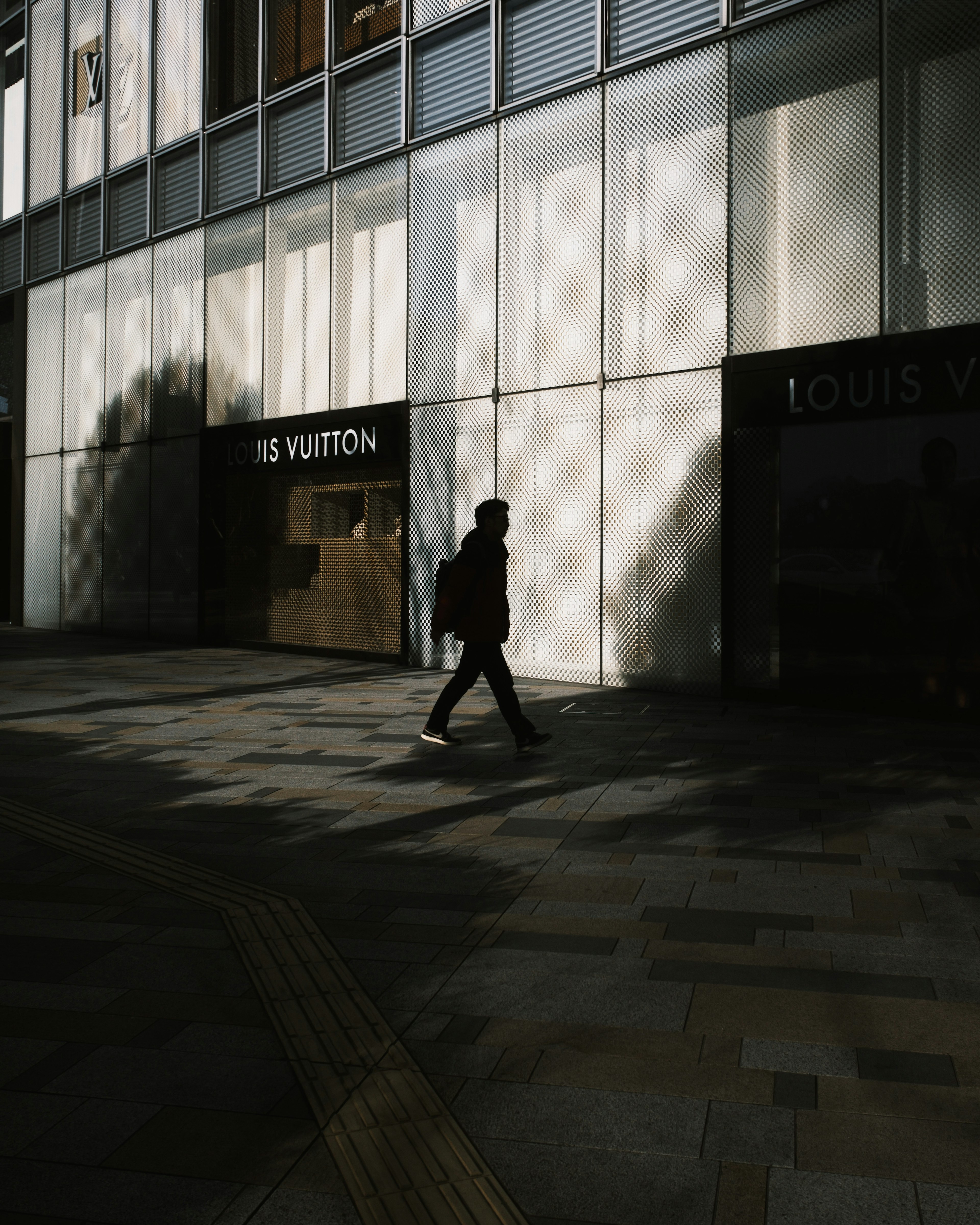 Silhouette einer Person, die vor dem Louis Vuitton-Geschäft mit Schattenmustern läuft