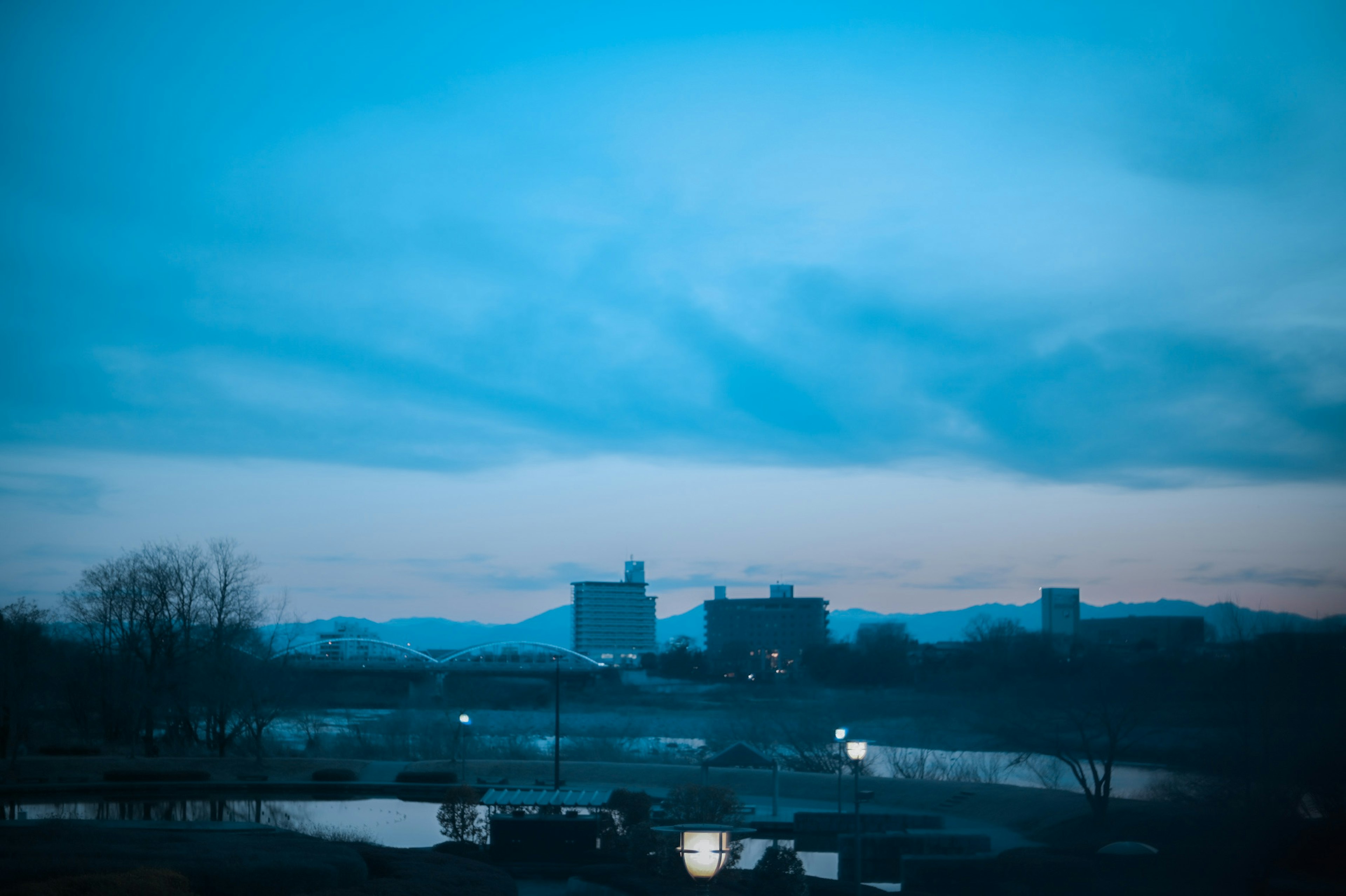 青い空と山を背景にした都市の風景 夕暮れ時の静かな湖と都市のシルエット