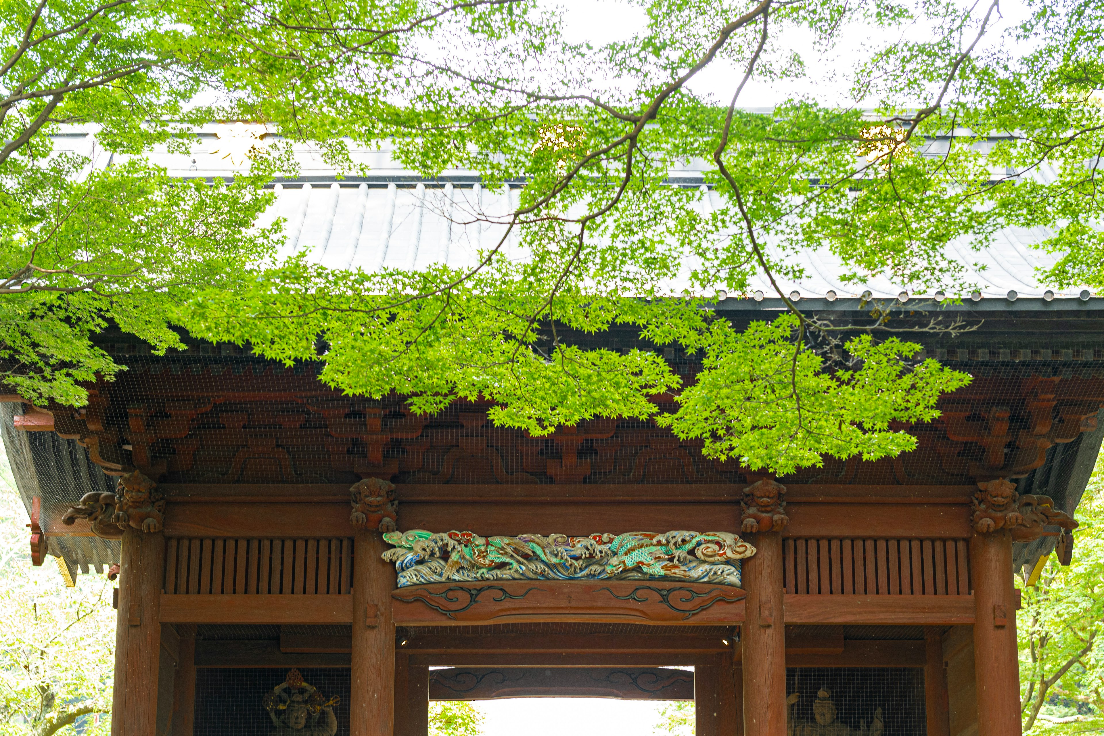 Traditional Japanese gate adorned with green leaves and intricate wooden carvings