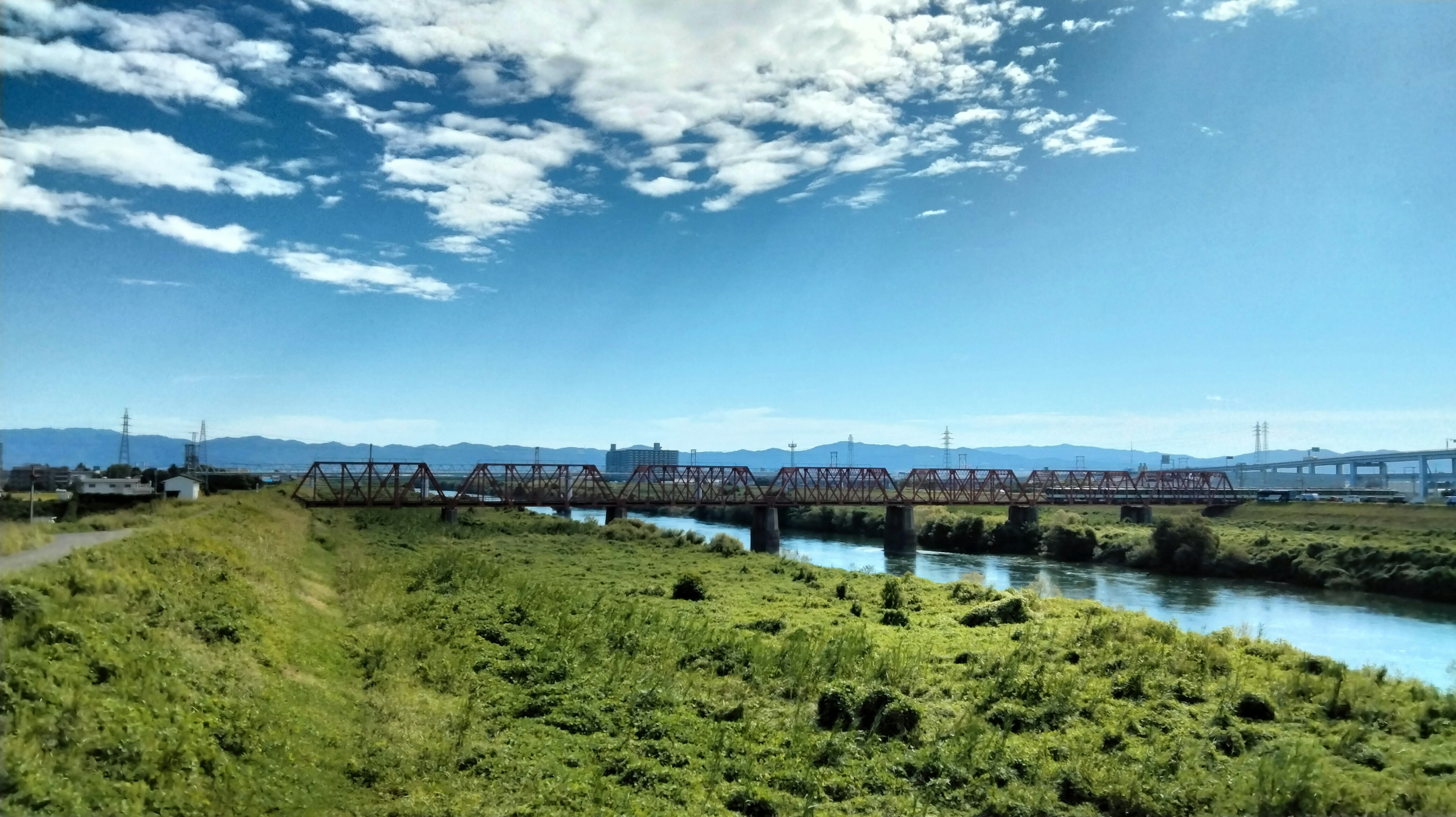 Pemandangan jembatan di atas sungai dengan rumput hijau dan langit biru