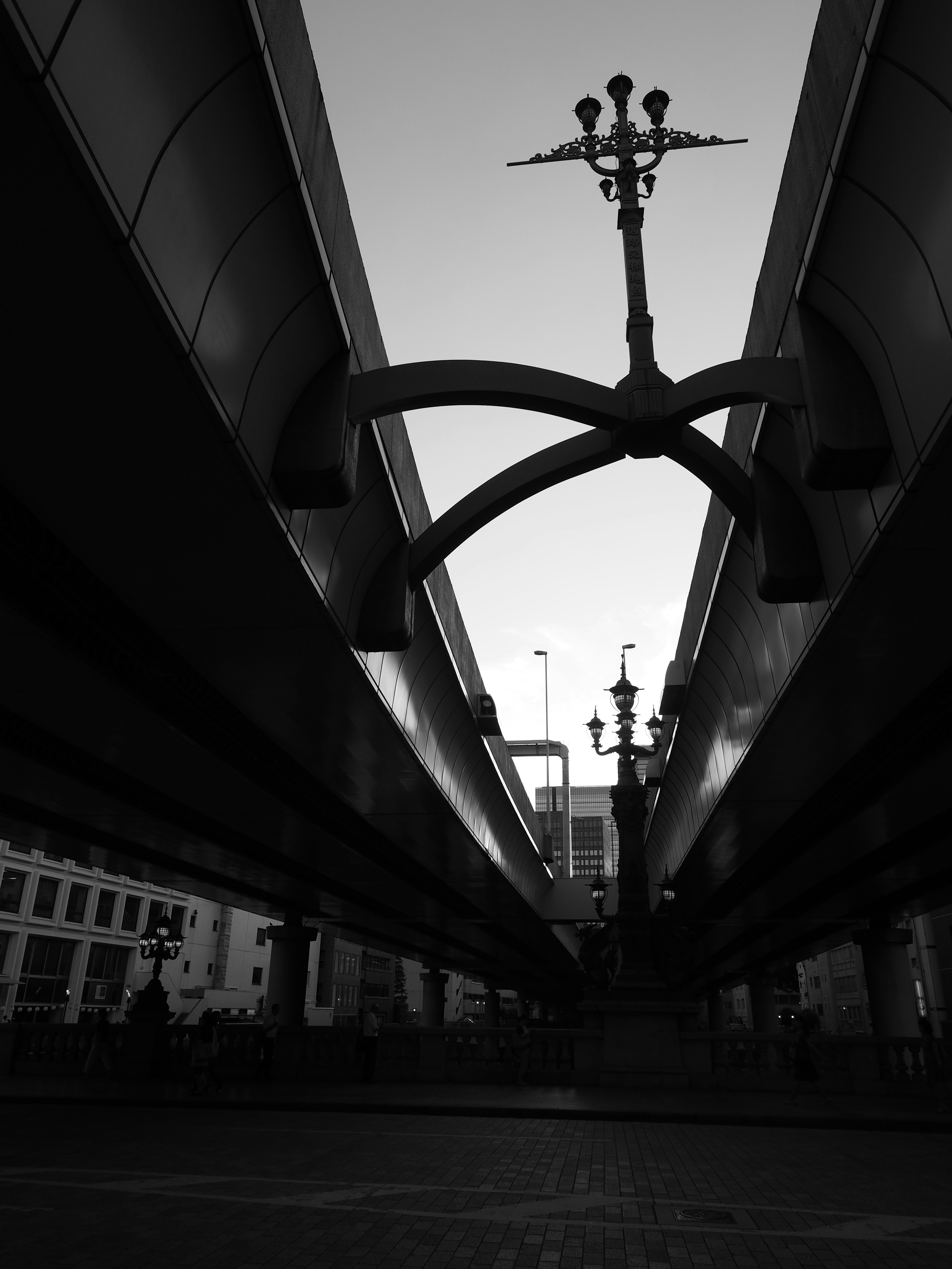 Silhouette of a structure viewed from beneath a bridge with street lamp