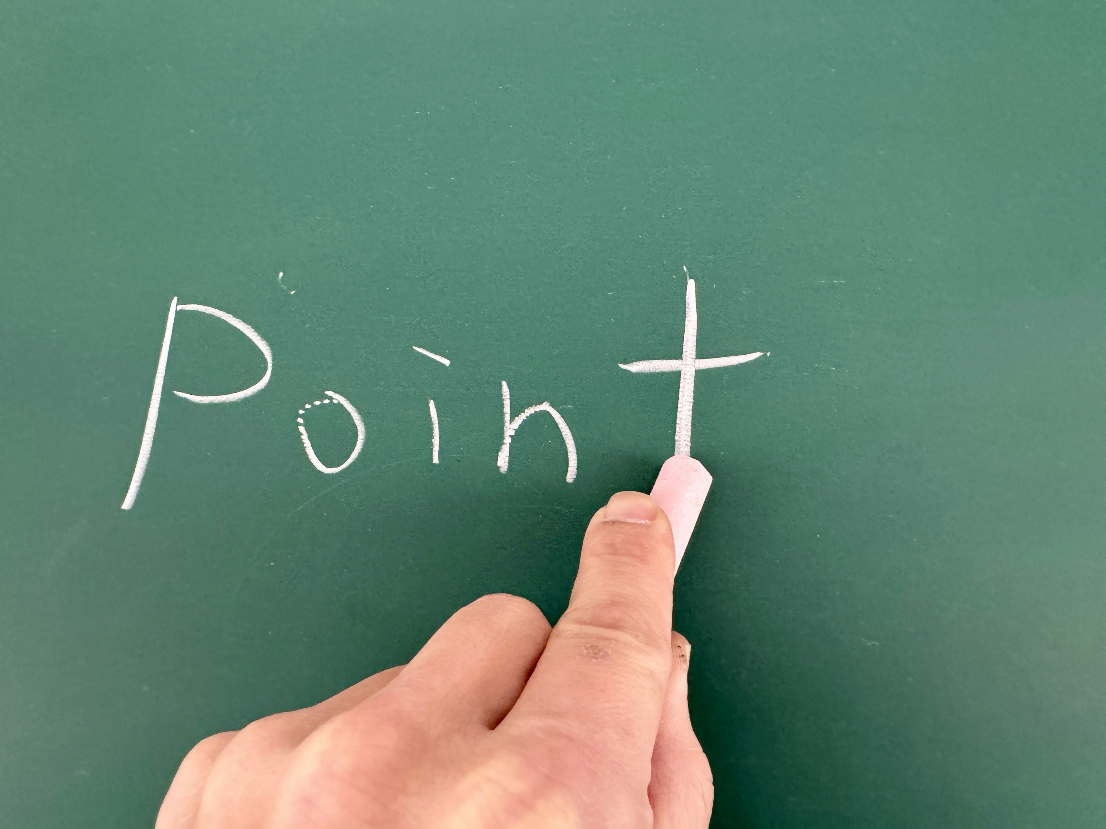 A hand pointing at the word Point written in white chalk on a green chalkboard