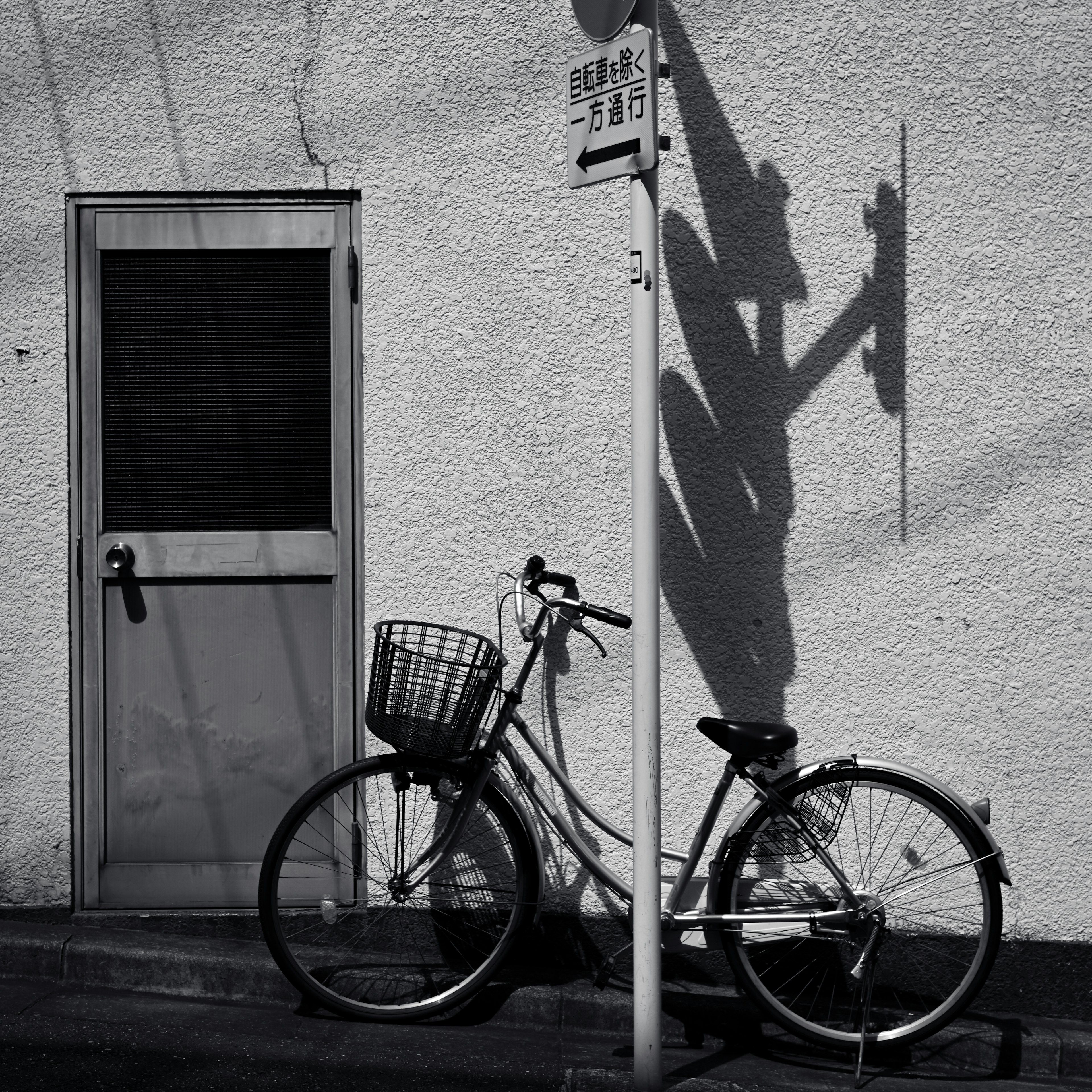 Una bicicleta en blanco y negro apoyada contra una pared con la sombra de una señal de tráfico