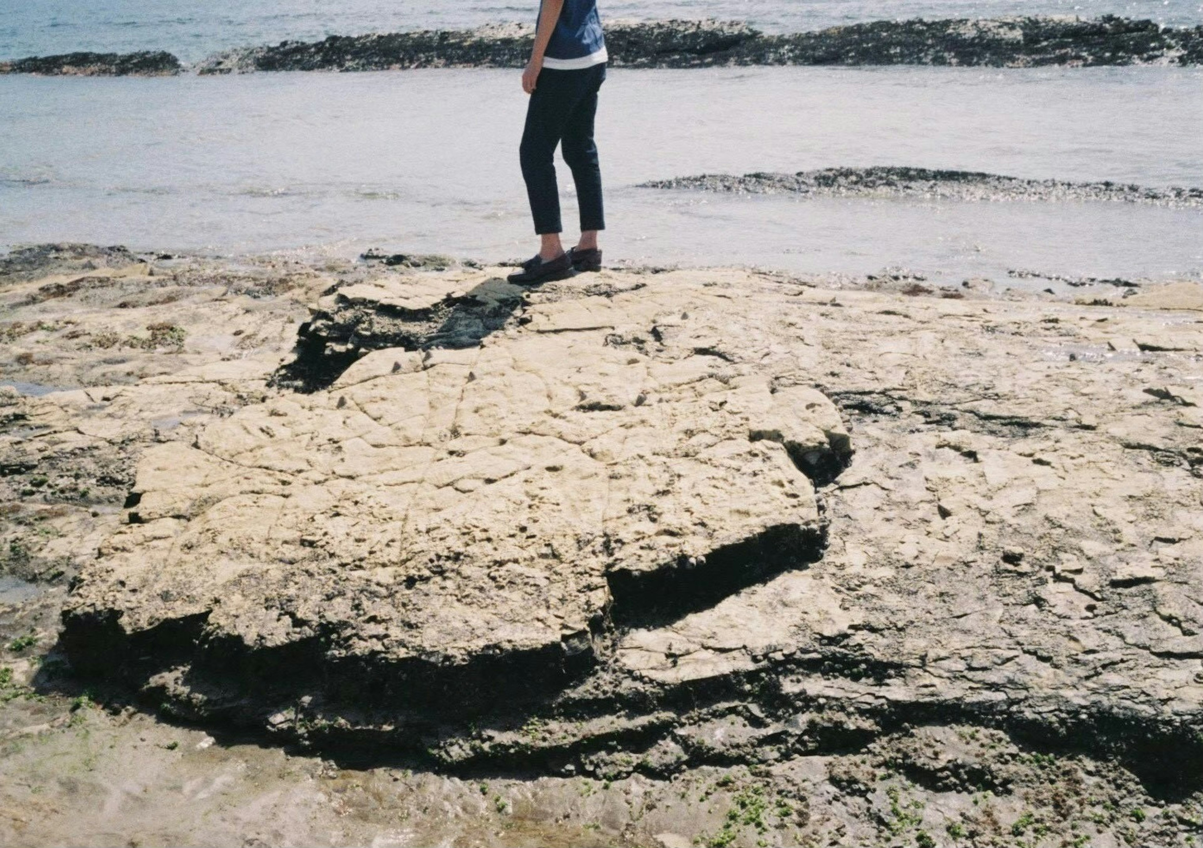 Person steht auf einer Küstenfelsformation am Meer