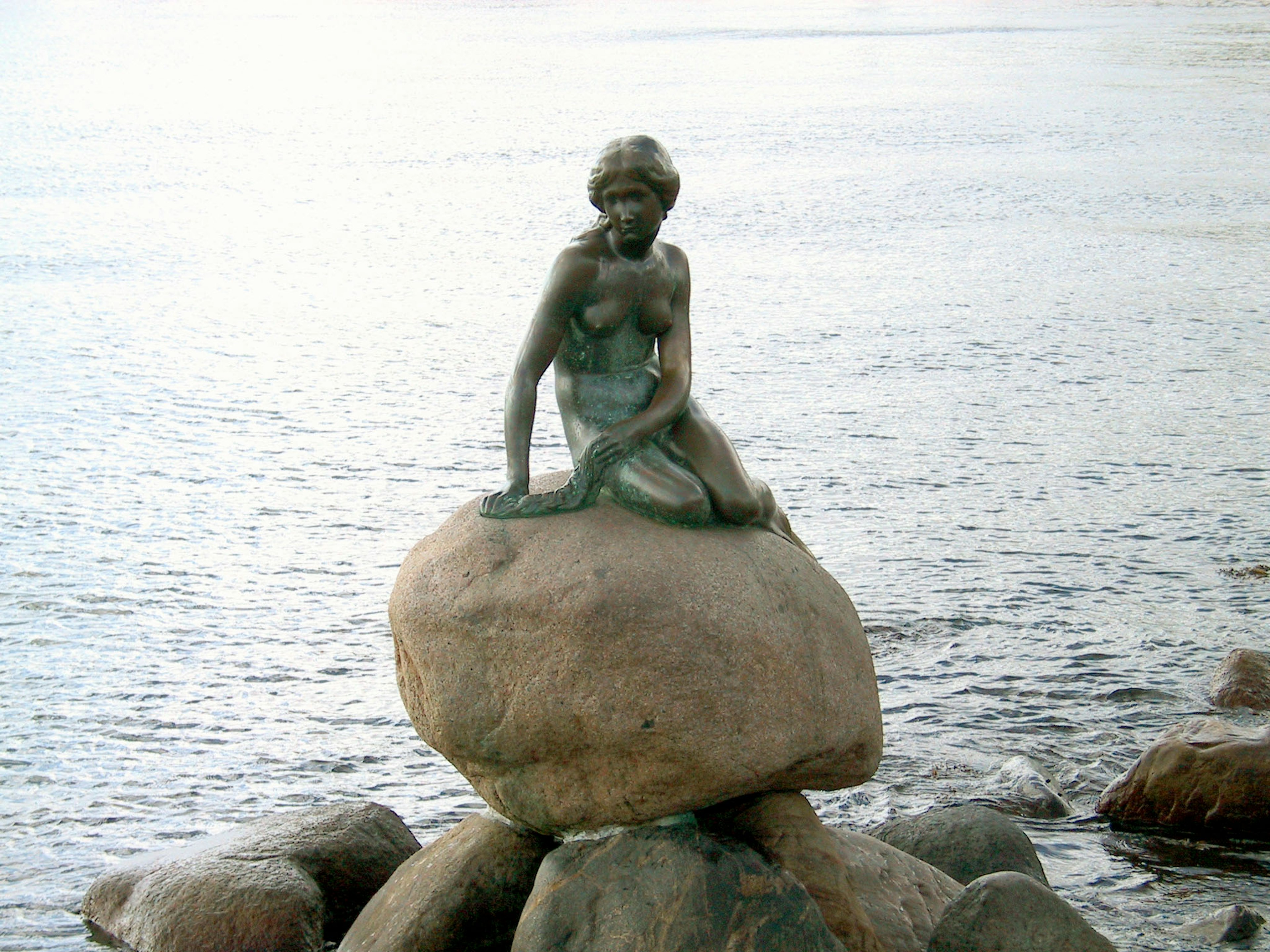 La statue de la Petite Sirène assise sur un rocher au bord de la mer