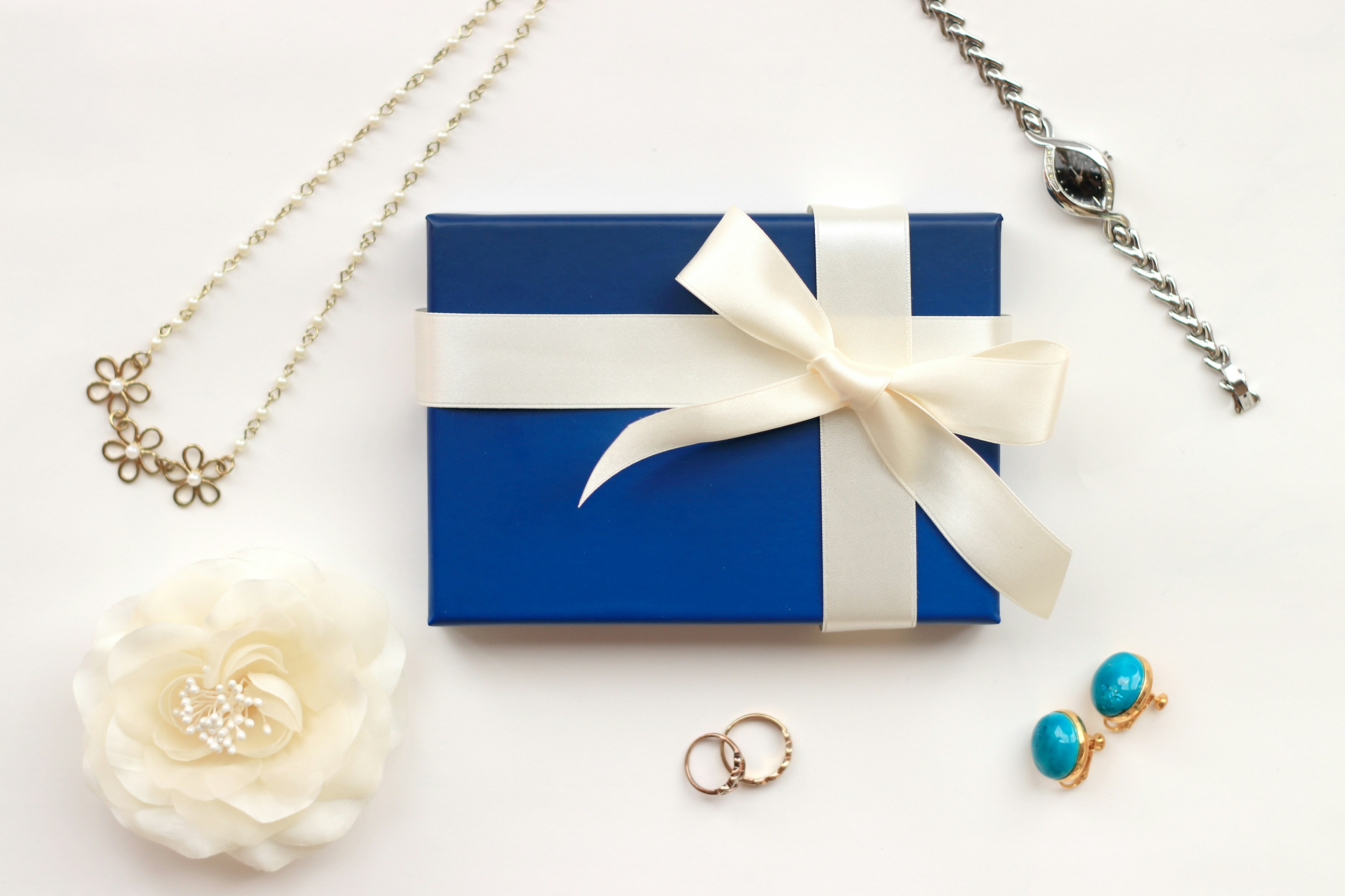 A blue gift box with a white ribbon surrounded by various jewelry pieces