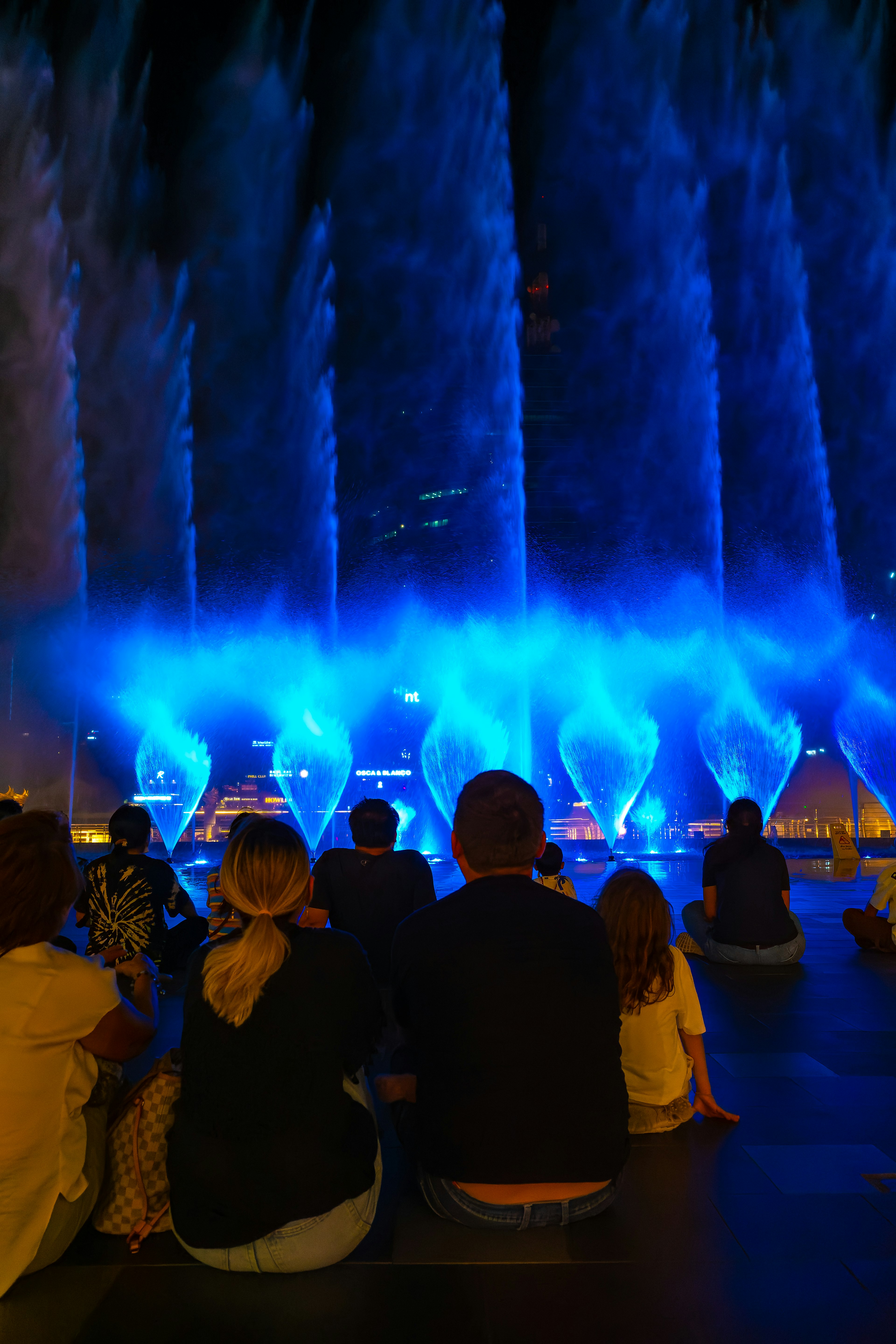 Silhouettes of people enjoying a blue fountain show