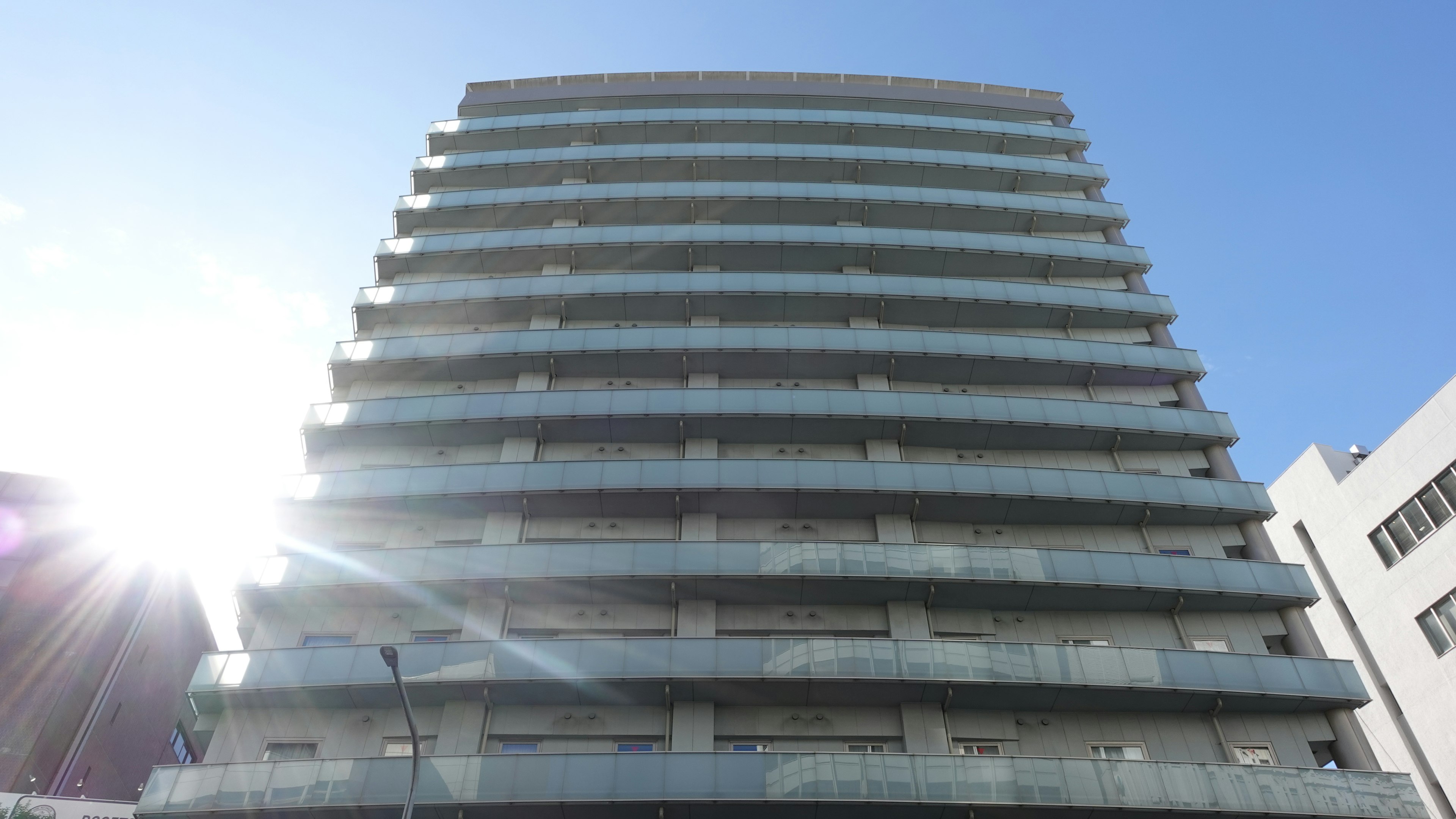 Modern high-rise building with glass balconies under a clear blue sky and sunlight