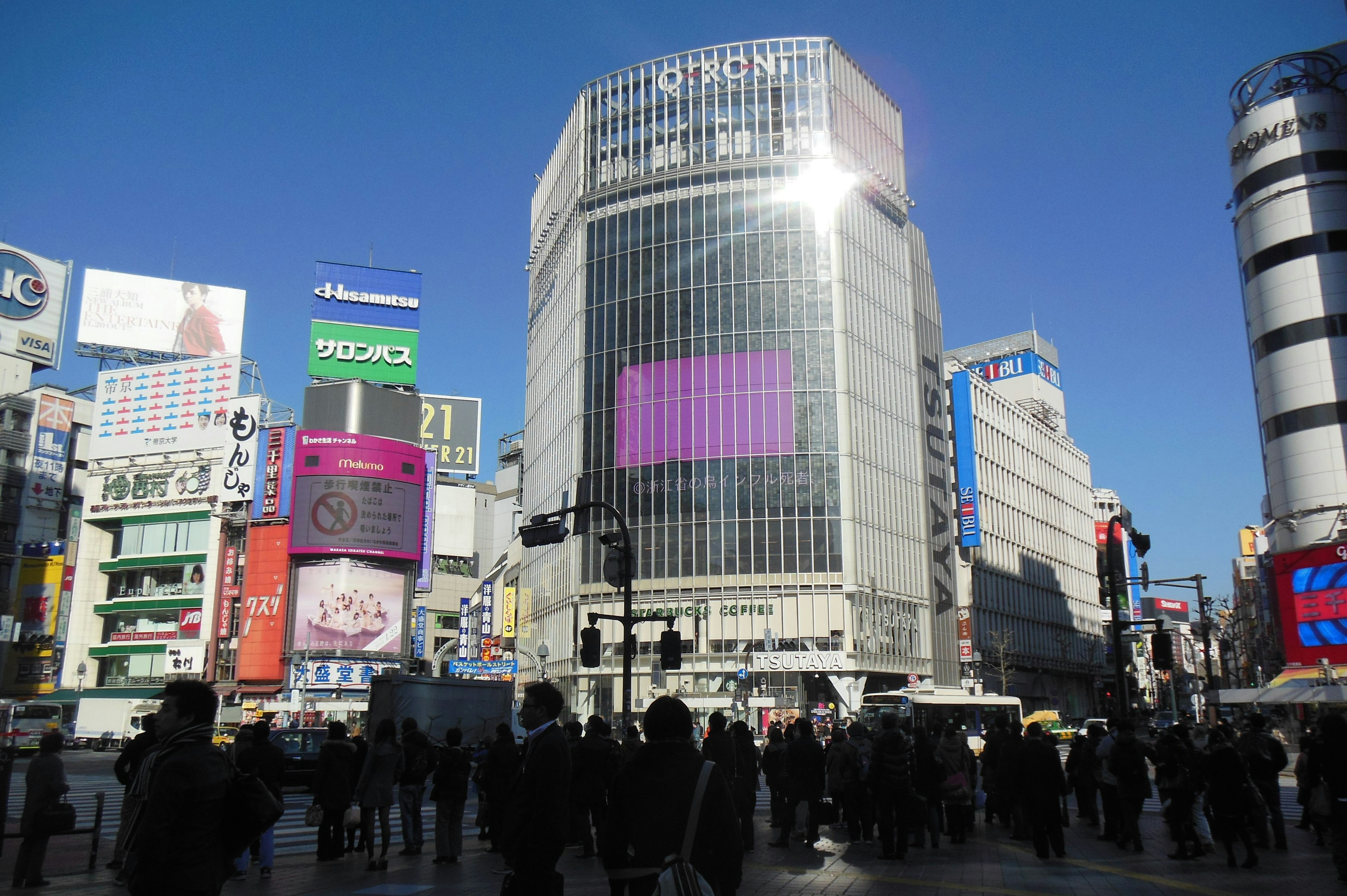 Persimpangan Shibuya dengan gedung tinggi dan kerumunan langit biru cerah dengan iklan besar