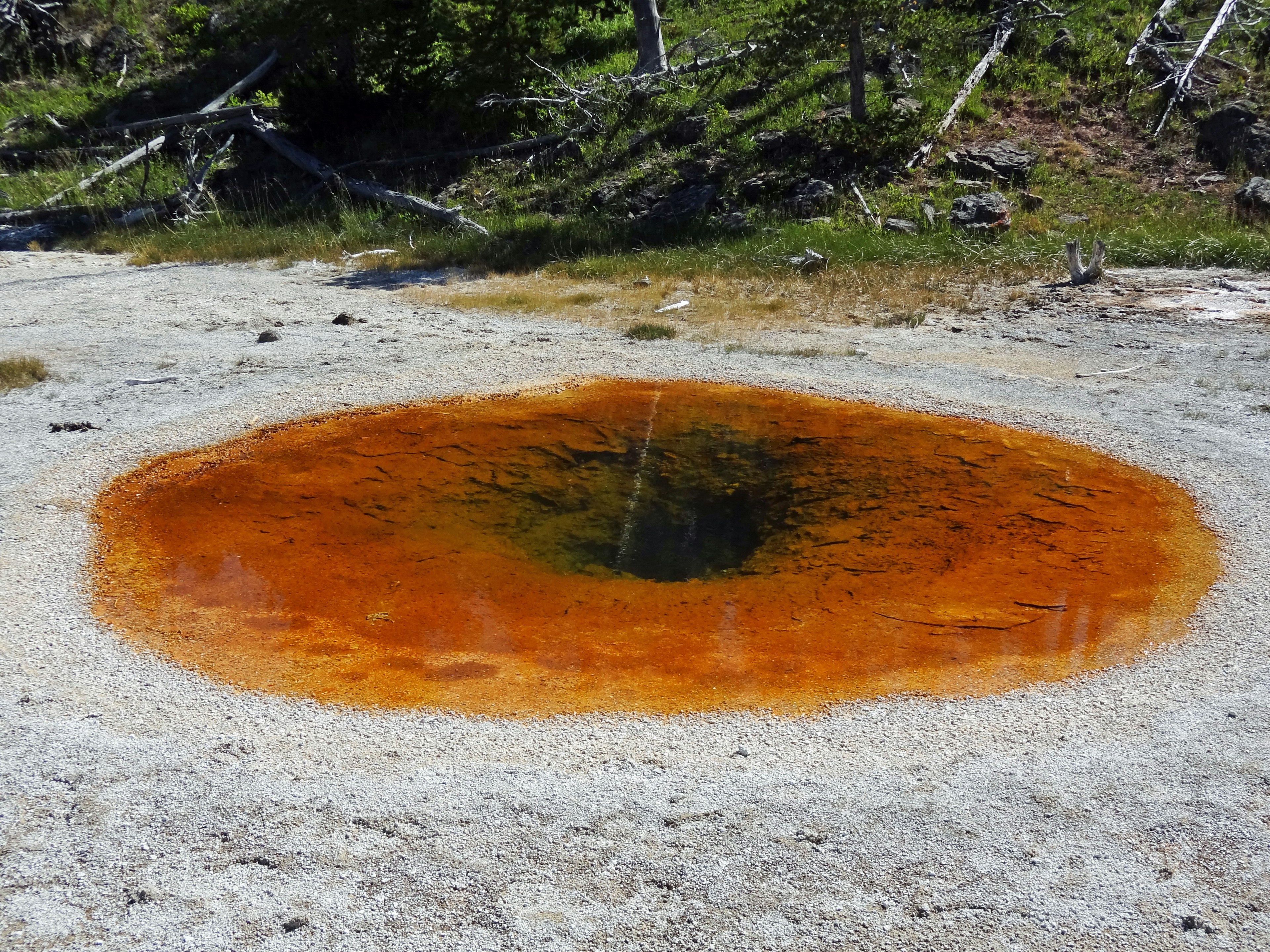 Pancuran air panas oranye dengan kolam dalam di tengah dan lanskap sekitarnya