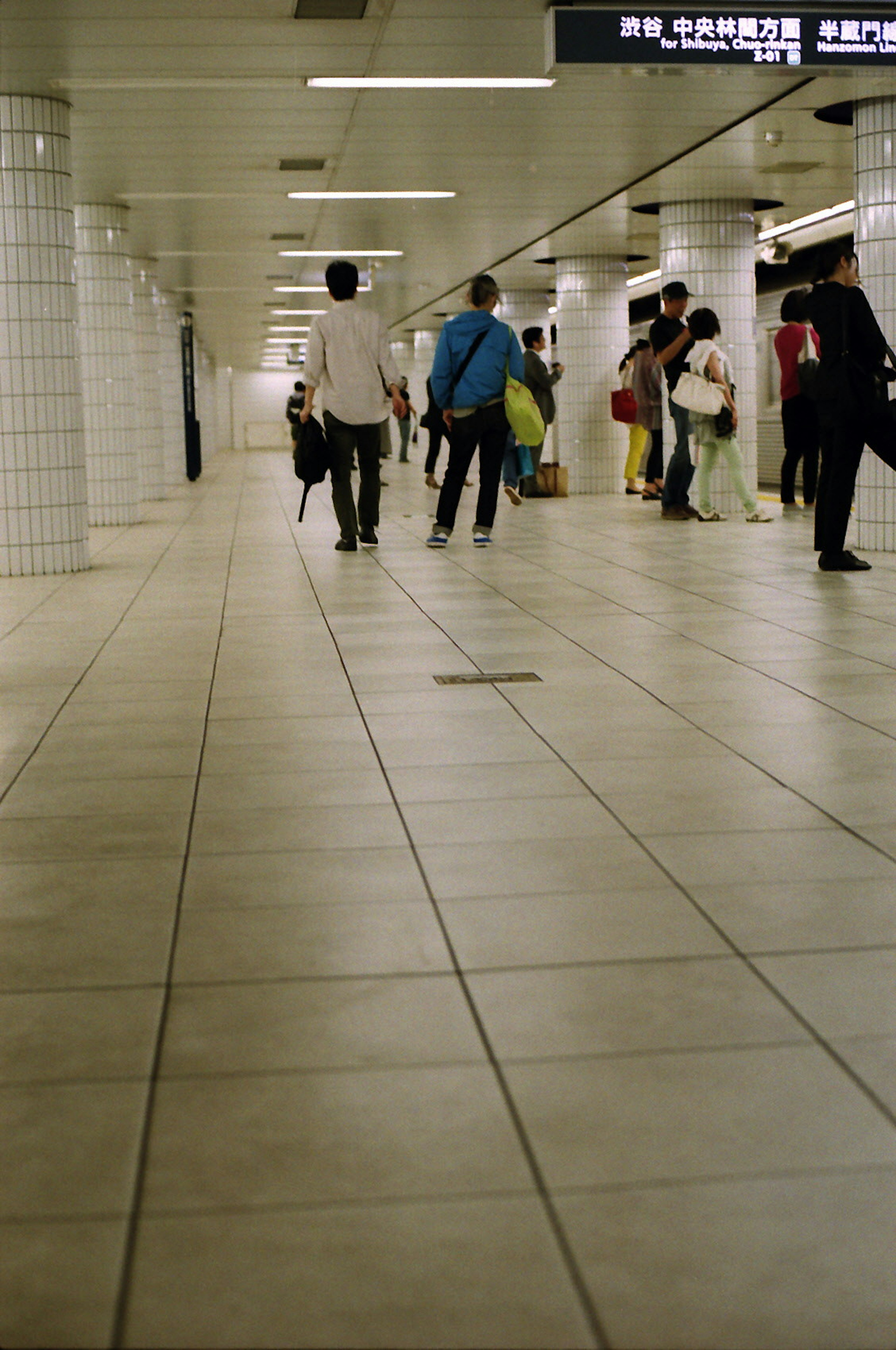 People walking in a subway station corridor with white tiled floor