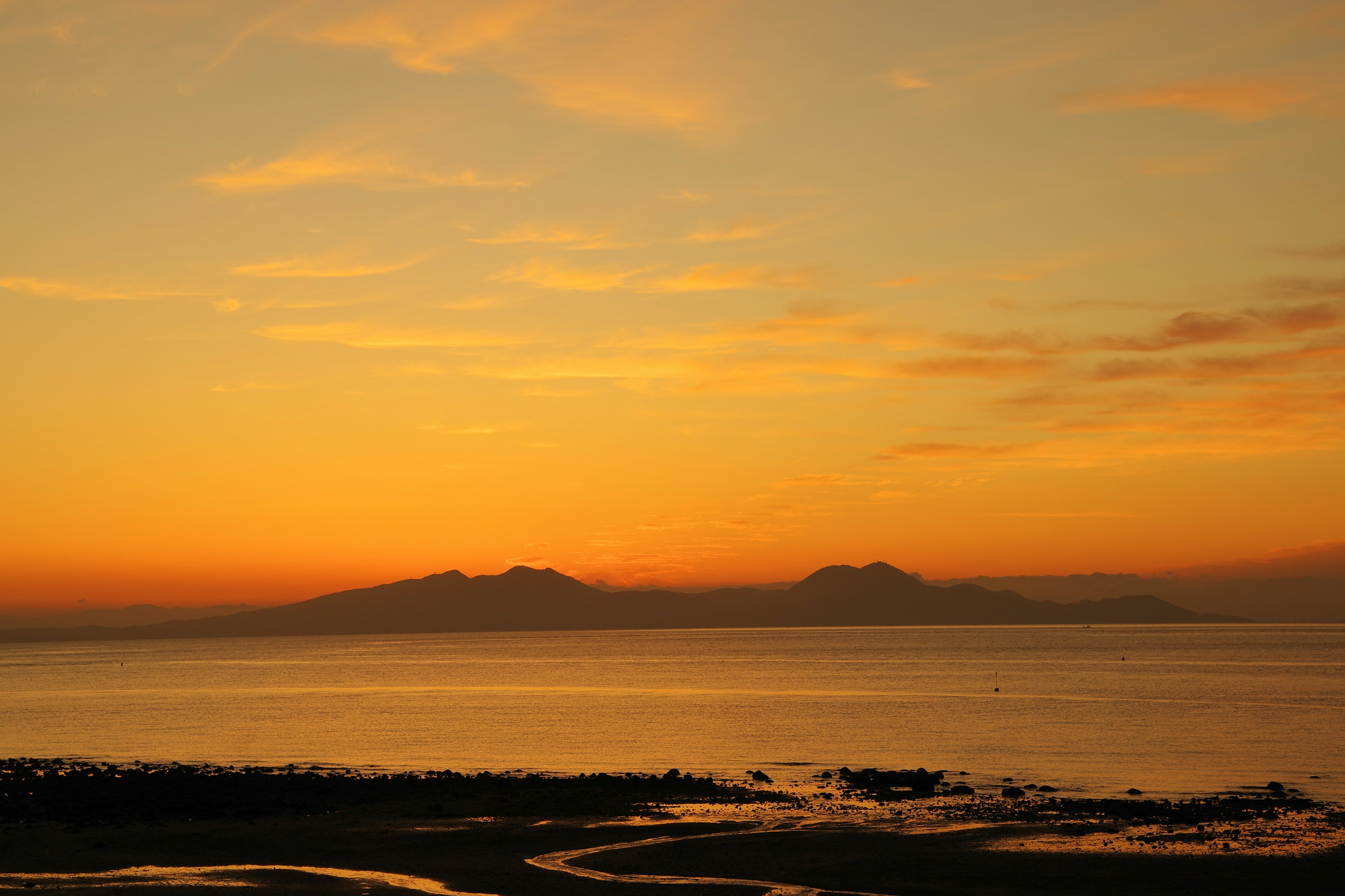 Sonnenuntergang über dem Ozean mit Silhouetten von Bergen