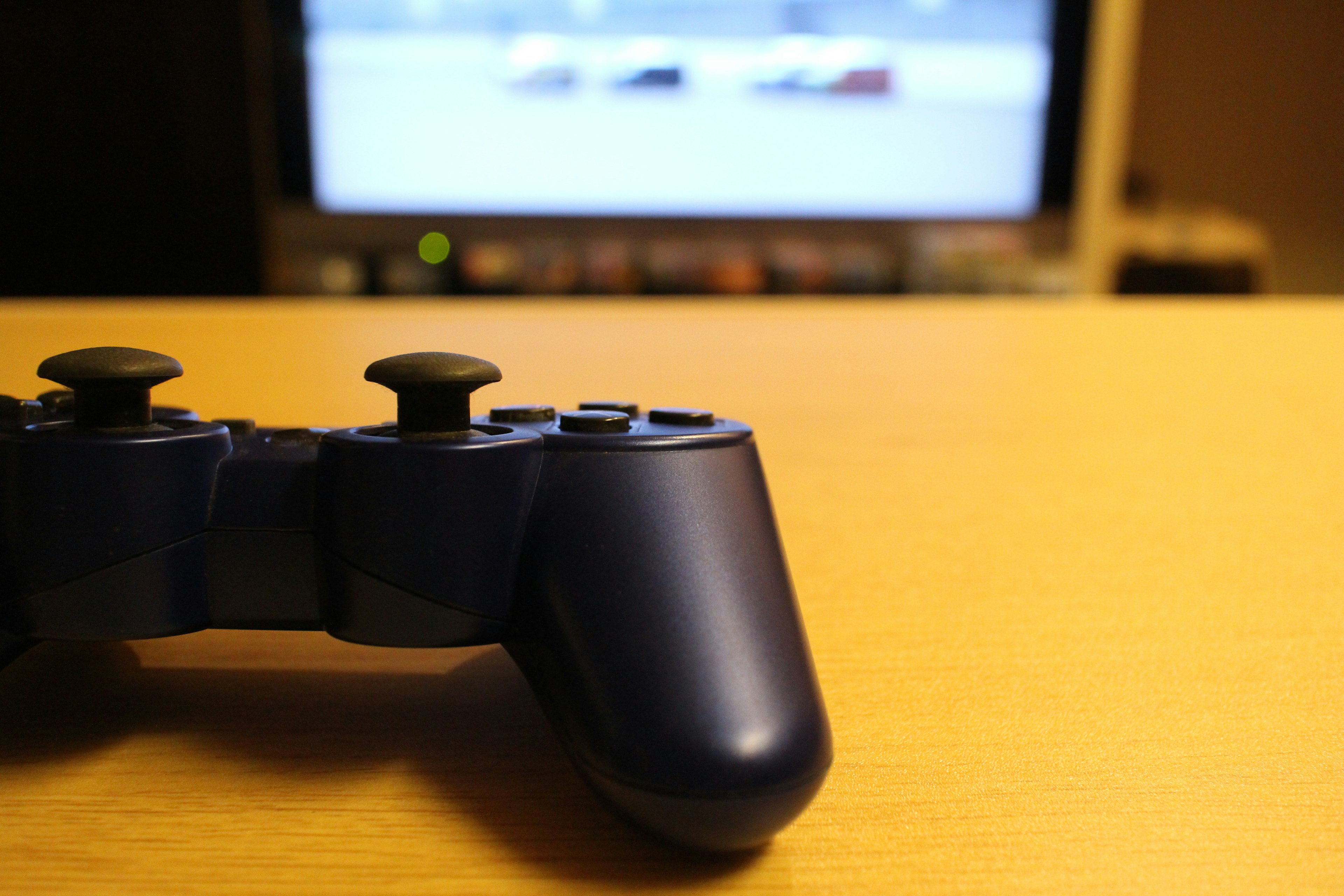 Controlador de juego azul sobre una mesa con una pantalla de televisión al fondo