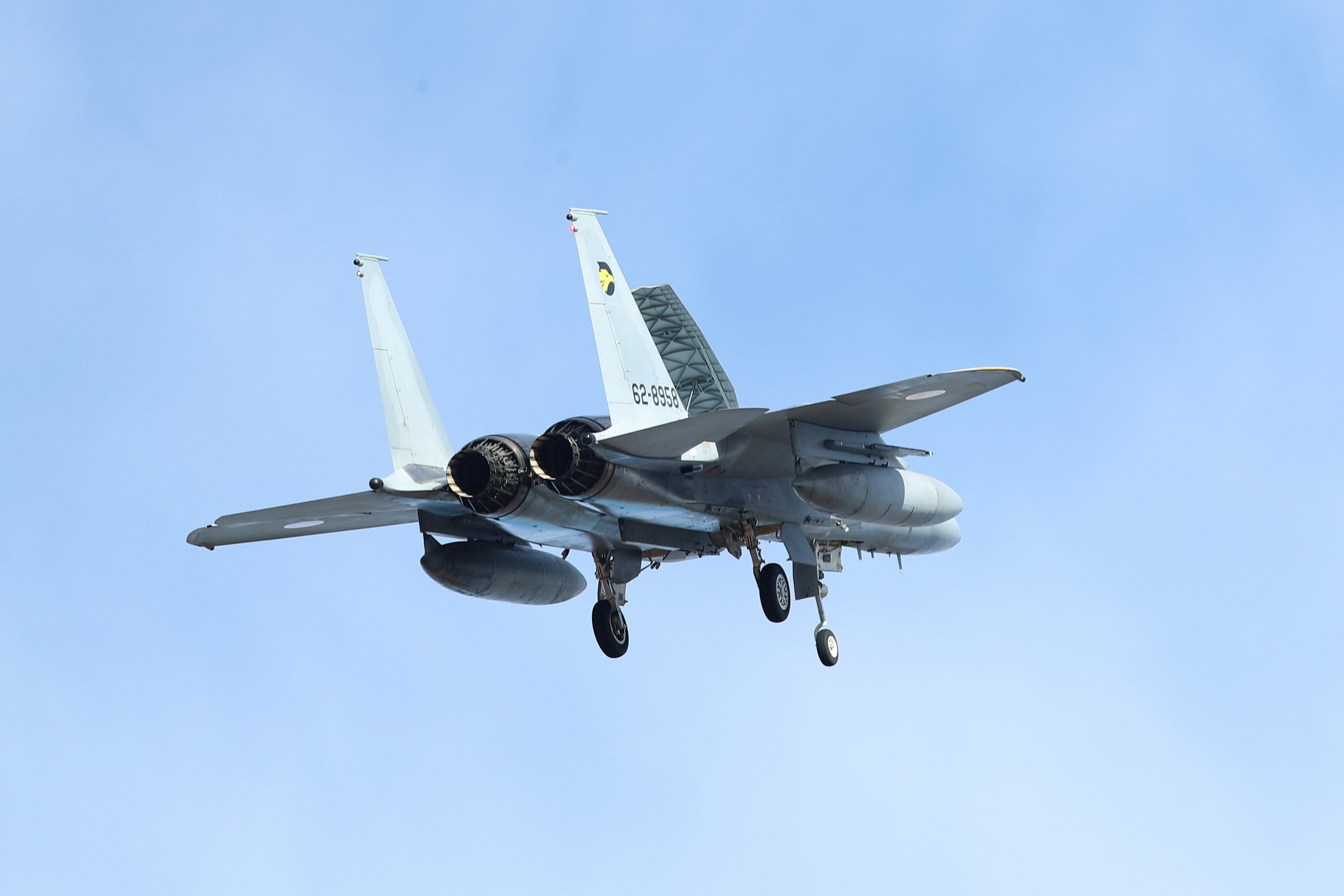 F-15 fighter jet flying against a blue sky from a rear perspective