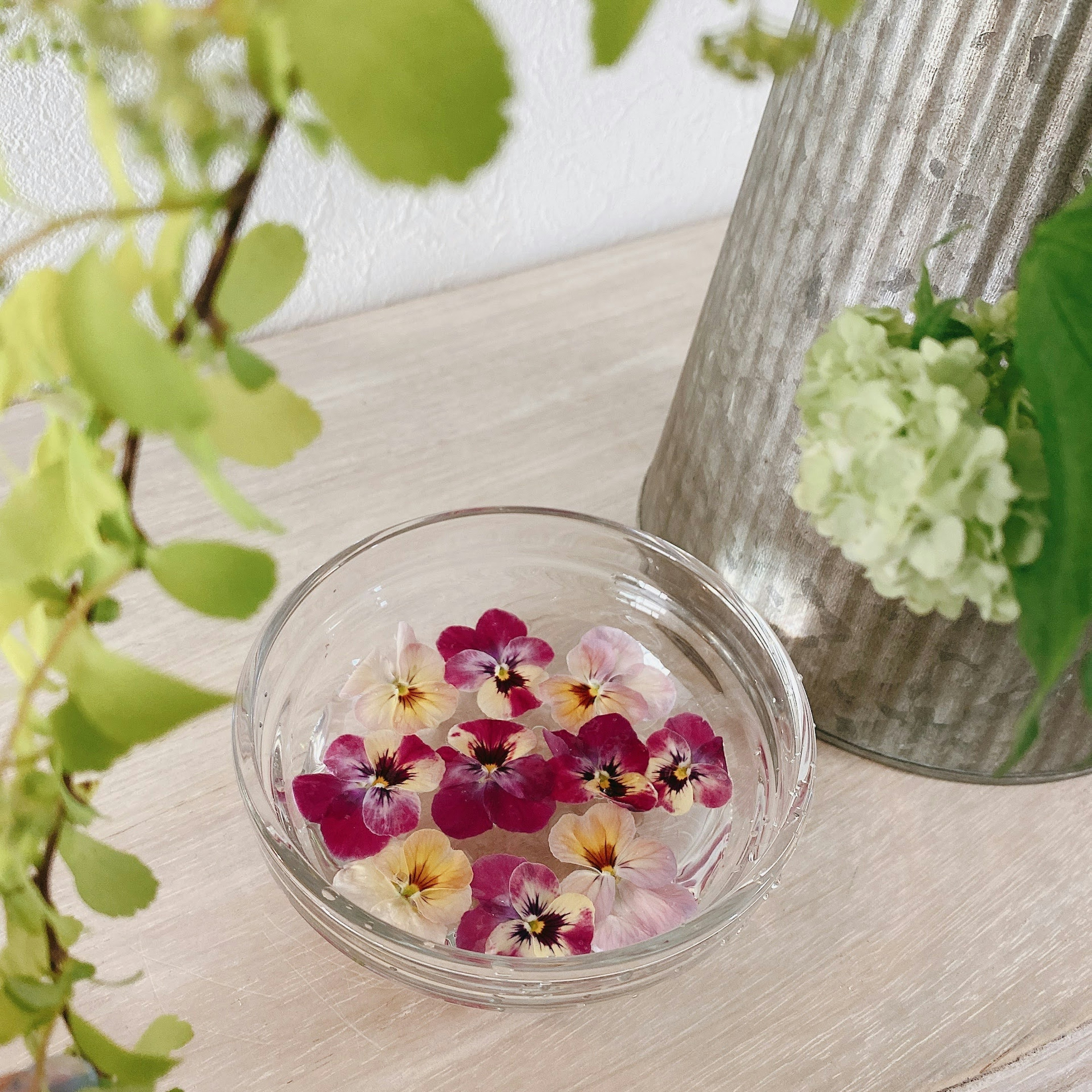 Bol transparent avec des pétales de fleurs violettes flottants à côté d'un vase en métal