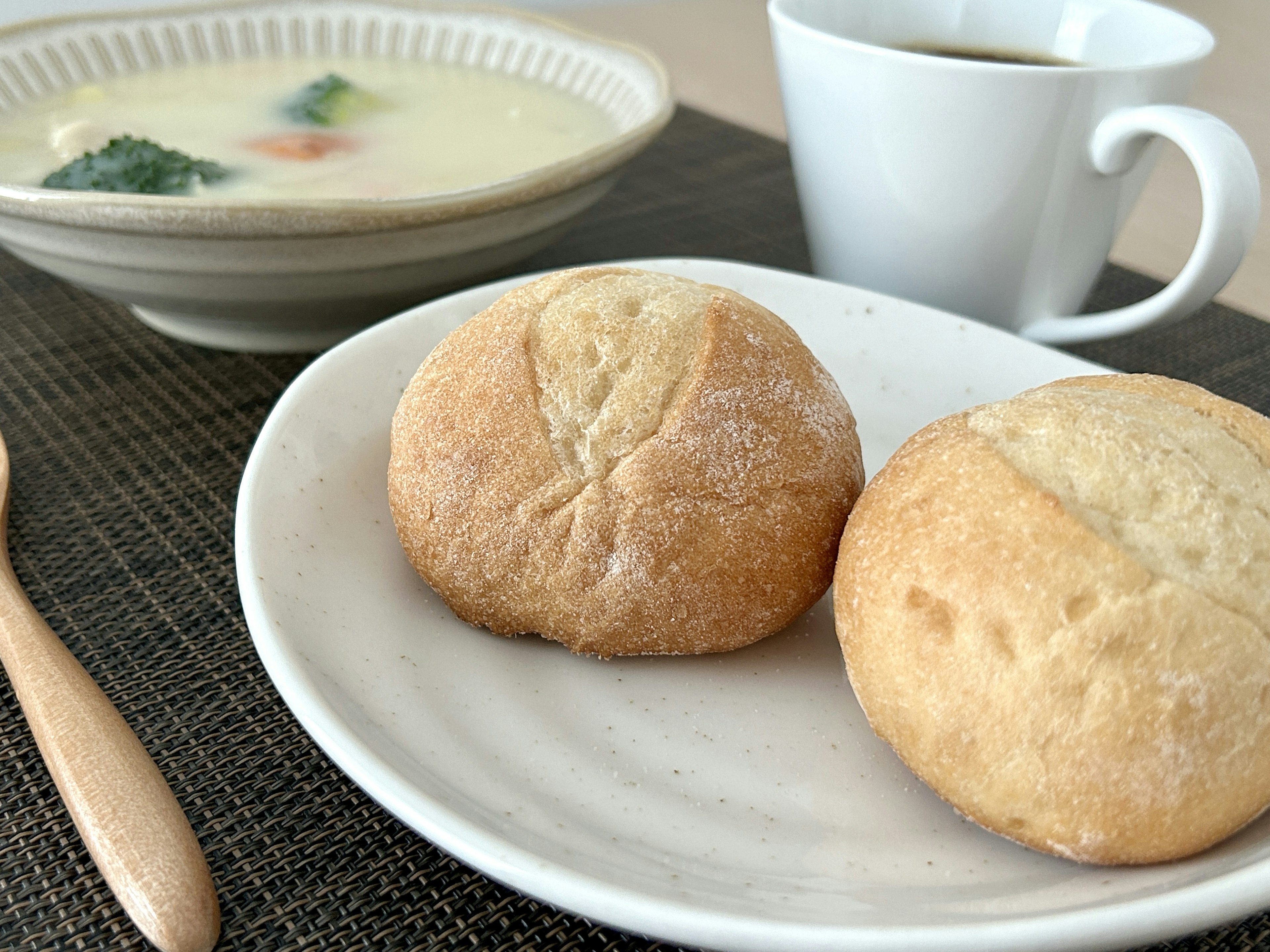 Zwei Brötchen auf einem weißen Teller mit einer Schüssel Suppe und einer Tasse Kaffee