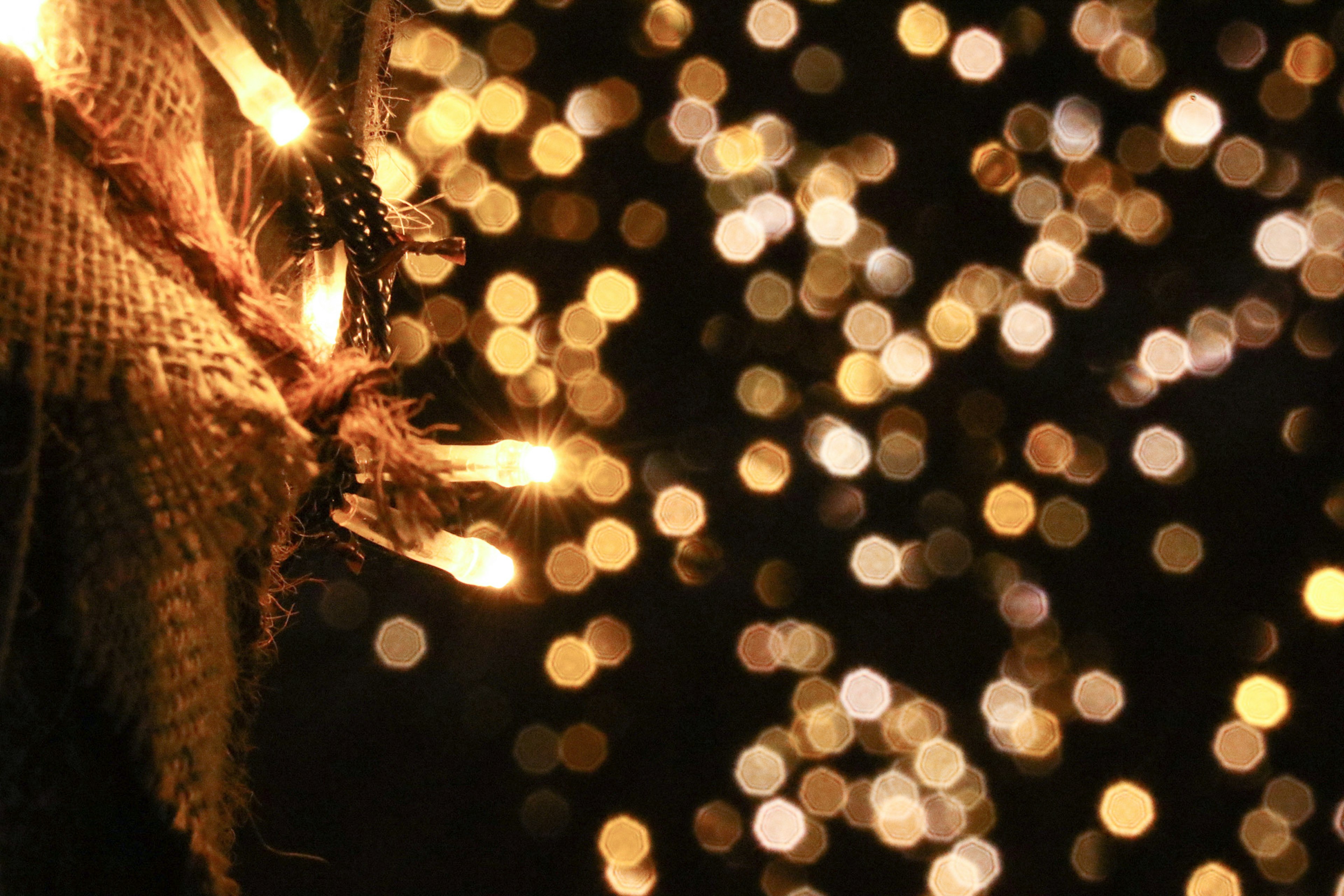 Gambar yang menampilkan lampu bokeh cerah di latar belakang gelap dengan sedikit kain goni