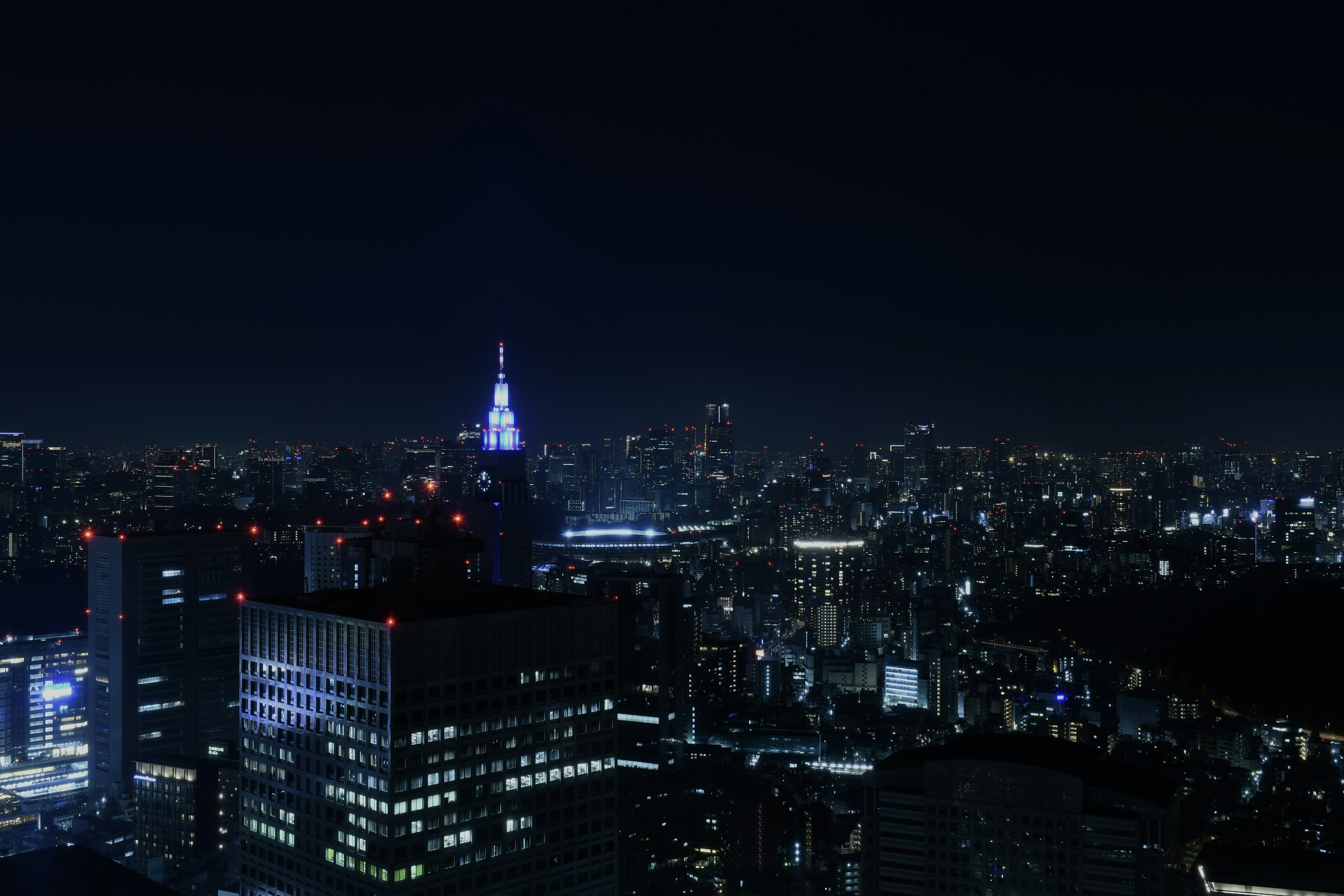 Tokyo skyline at night featuring skyscrapers and a blue illuminated tower