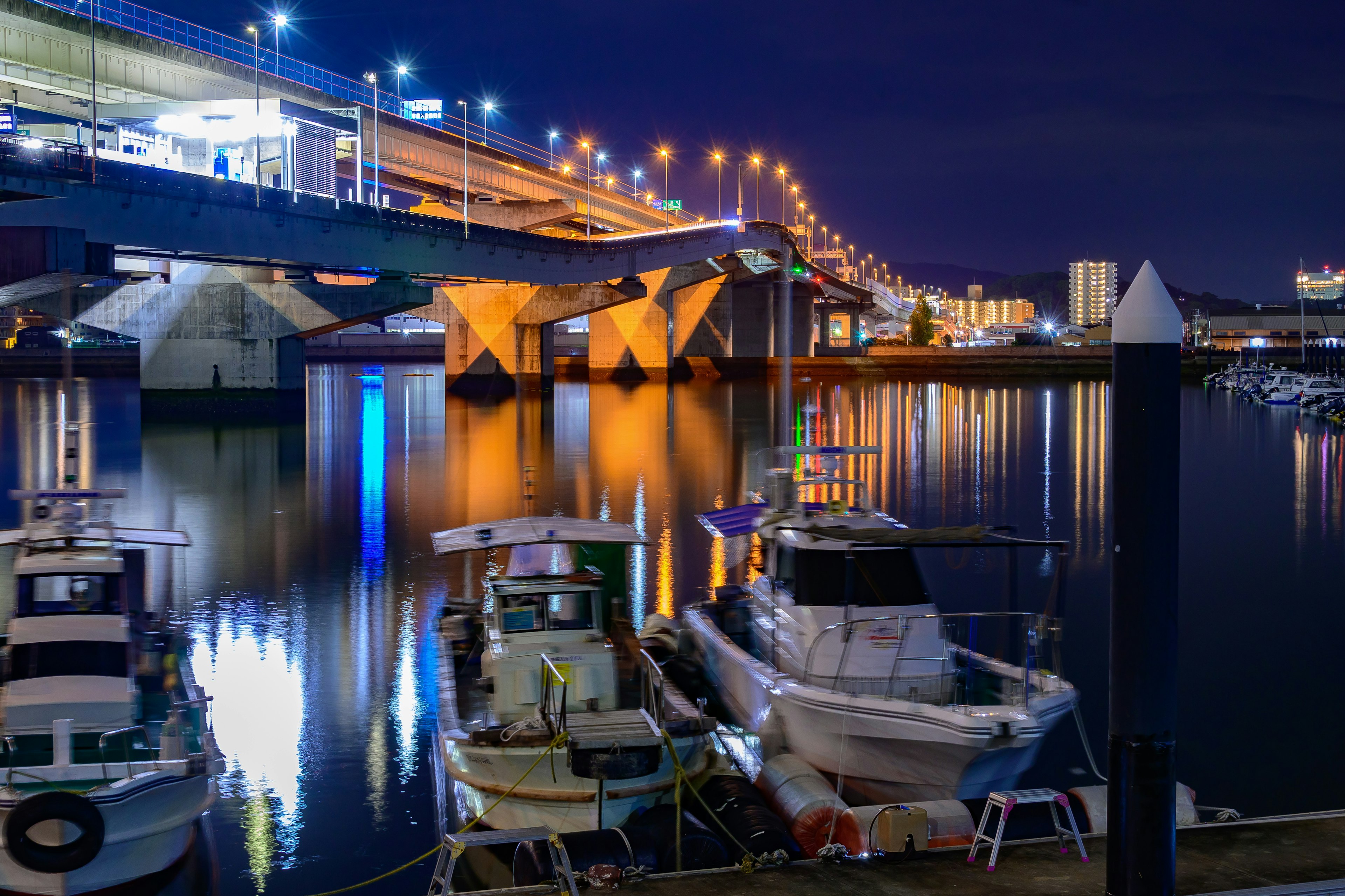 Perahu di malam hari di pelabuhan dengan jembatan yang memantul di air