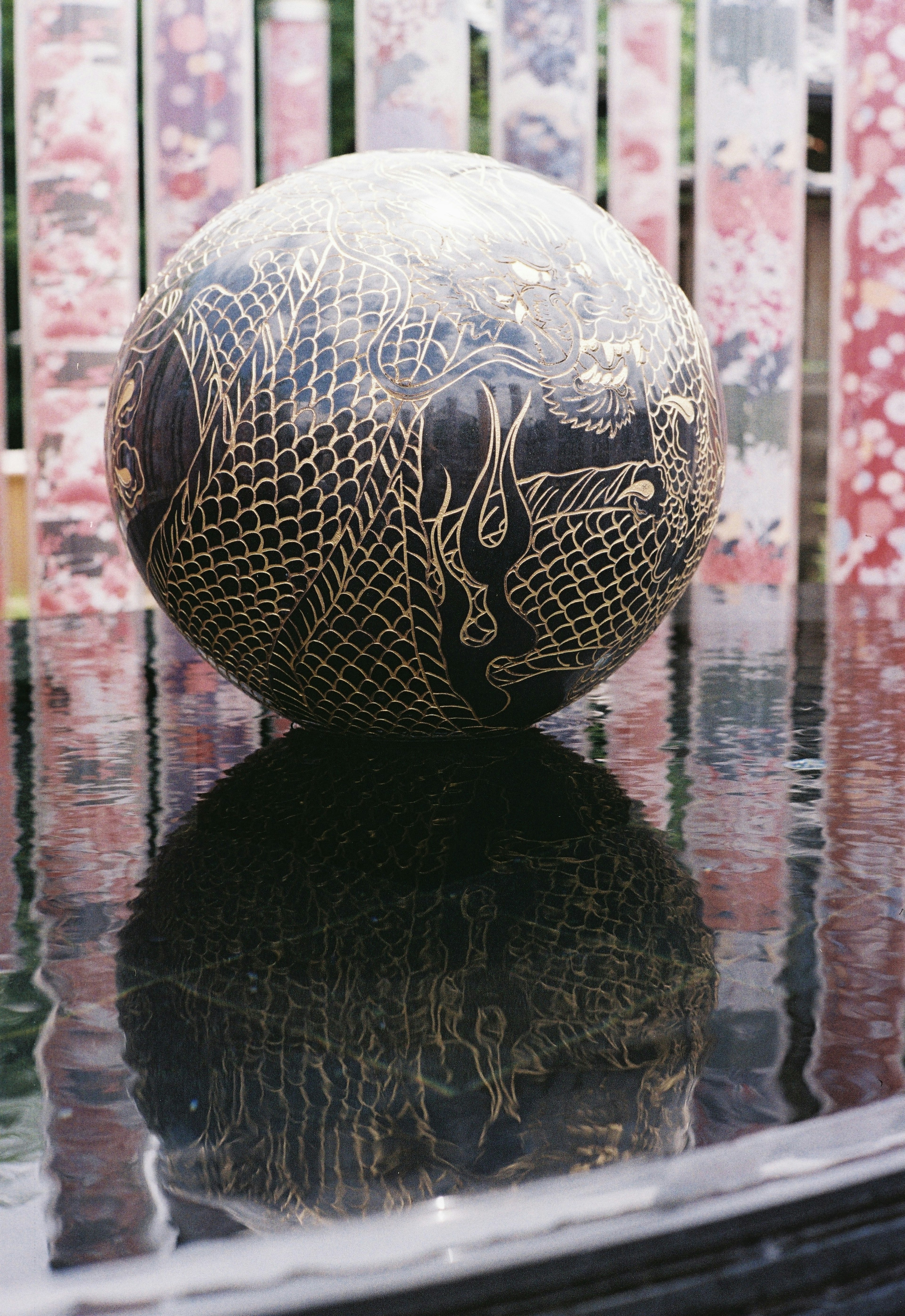 A round black sphere with intricate golden patterns reflecting on a surface