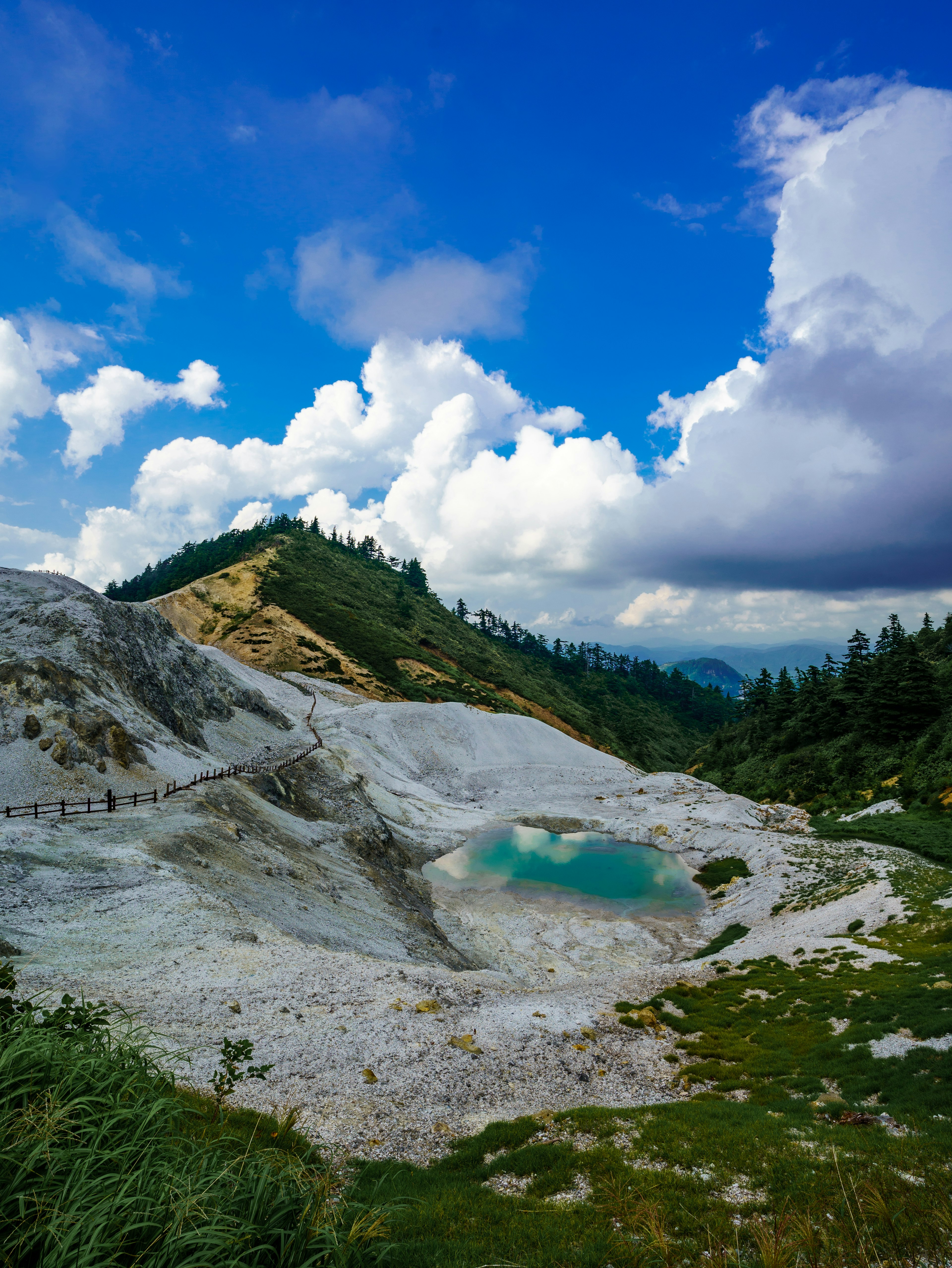 青い空と白い雲の下の美しい風景 緑の草と青い水の池がある山の斜面