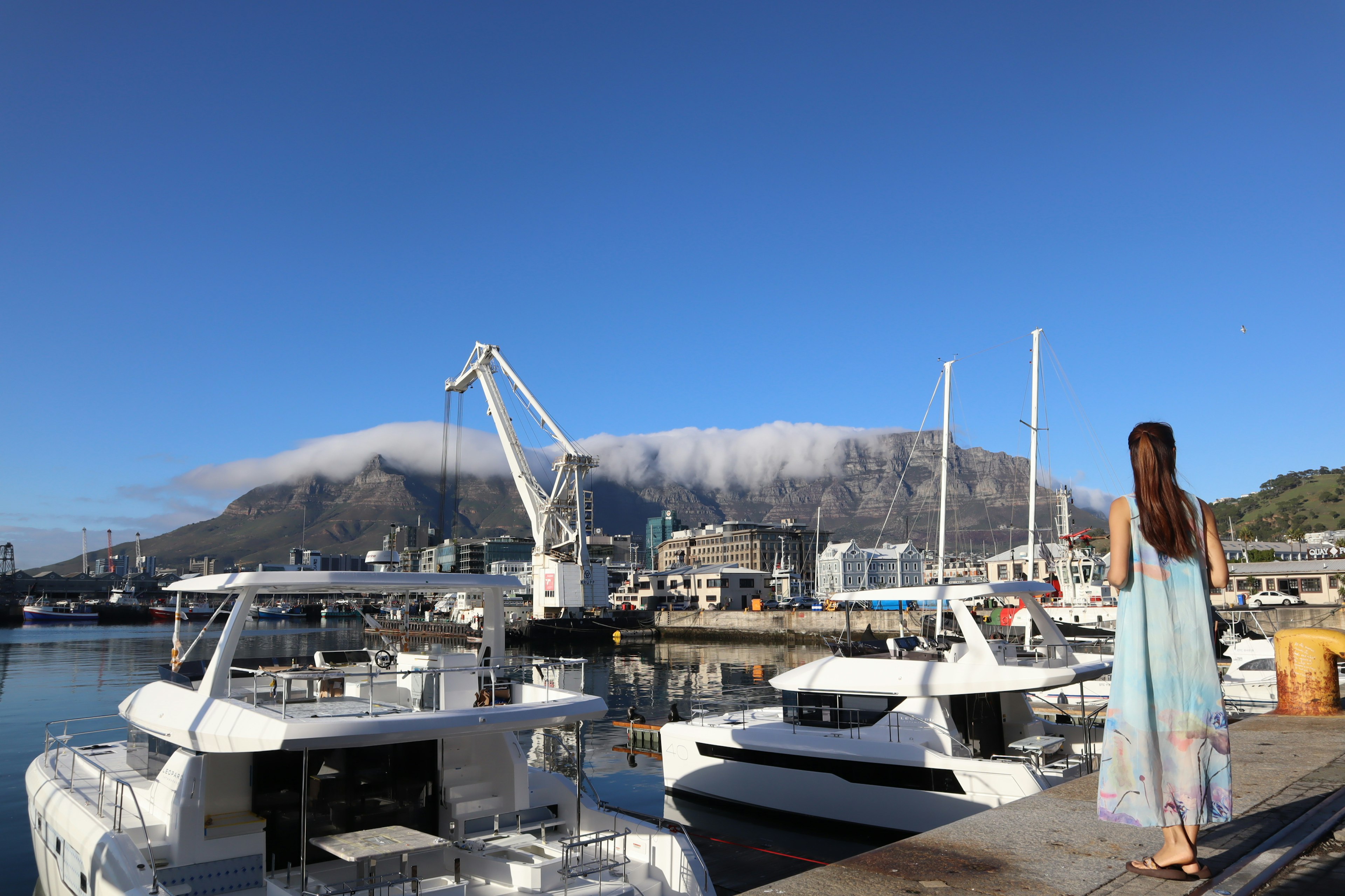 Frau, die Boote im Hafen betrachtet mit Bergen, die von Wolken bedeckt sind