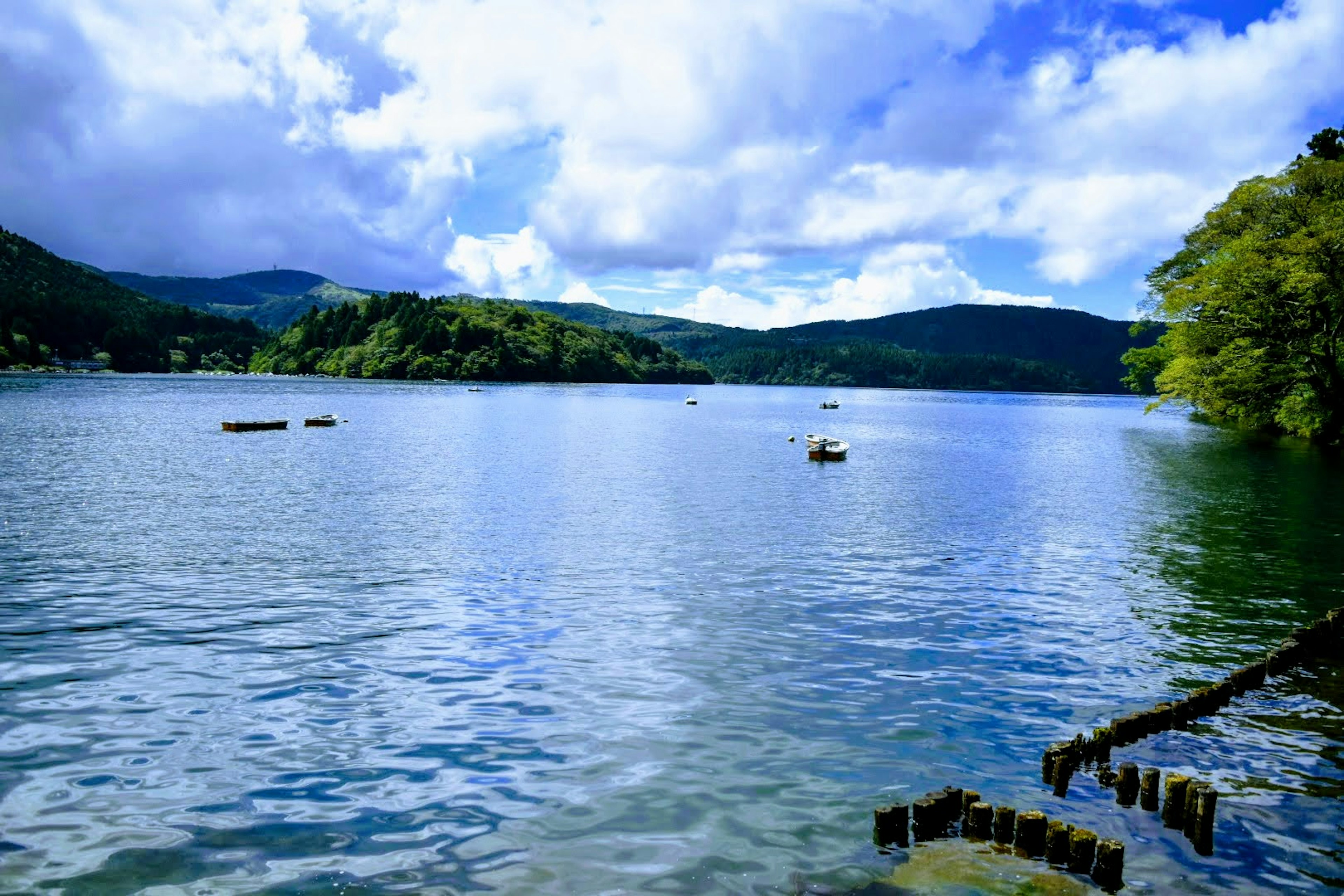 Vista panoramica di un lago blu circondato da montagne verdi Cielo luminoso con nuvole riflesse sulla superficie dell'acqua