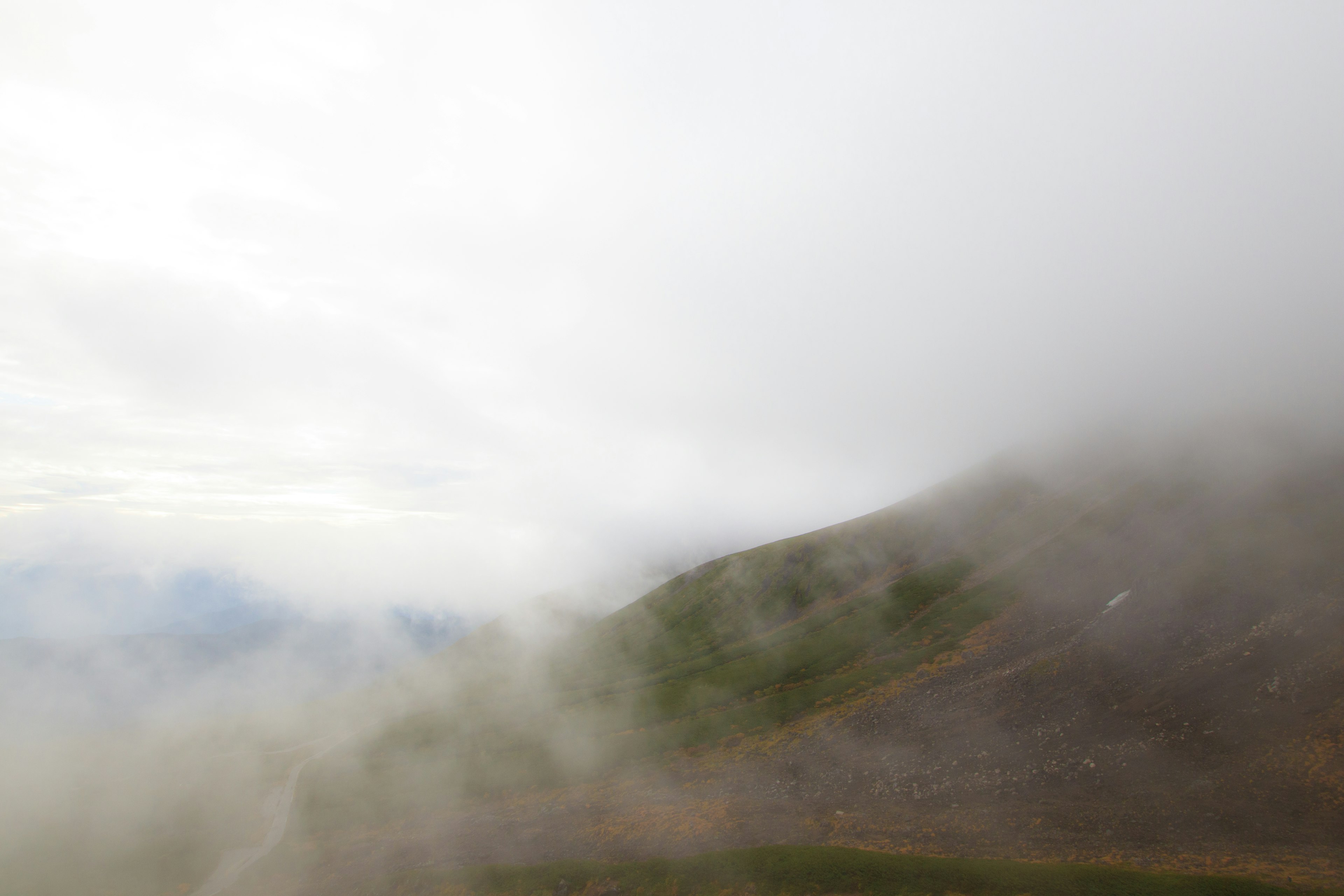 Paisaje montañoso envuelto en niebla con terreno cubierto de hierba y nubes