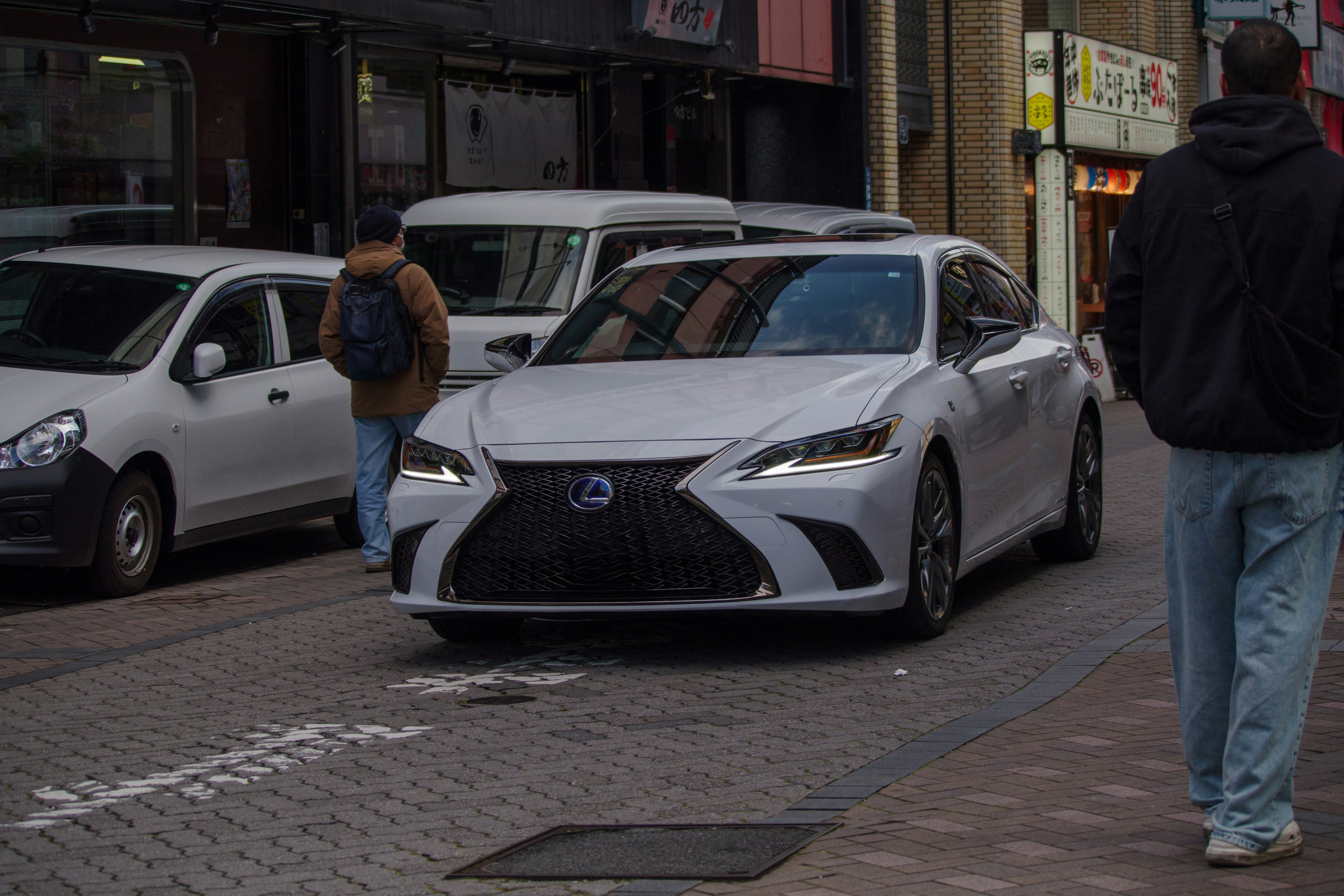 White Lexus car driving on a city street with pedestrians