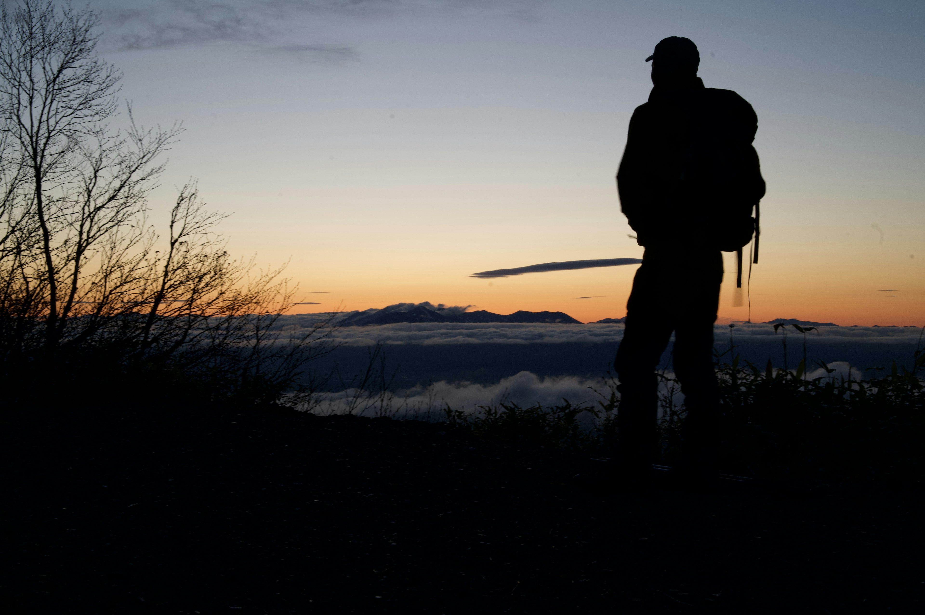 Silhouette of a man with a backpack standing against a sunset