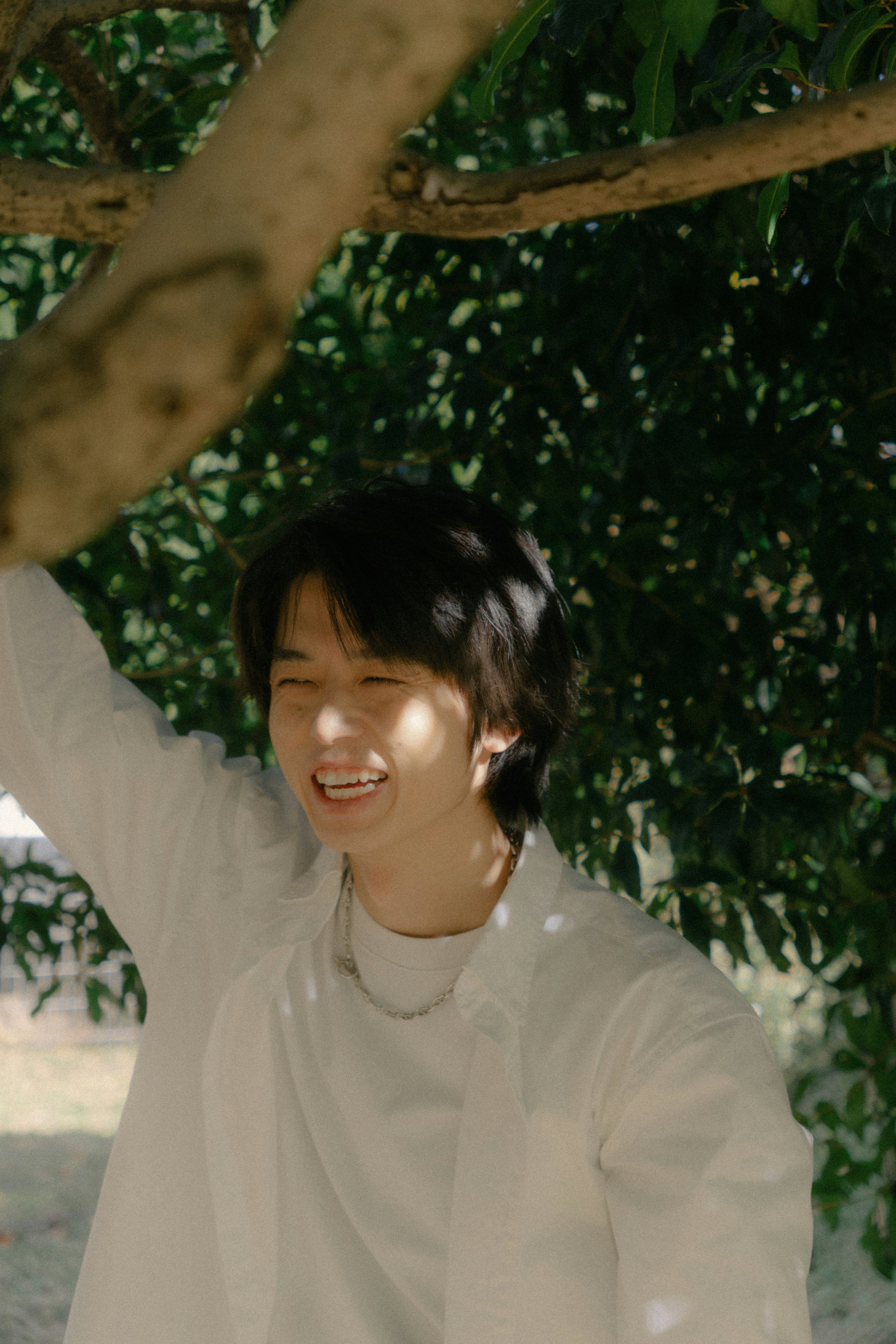 Young person smiling under a tree wearing a white shirt