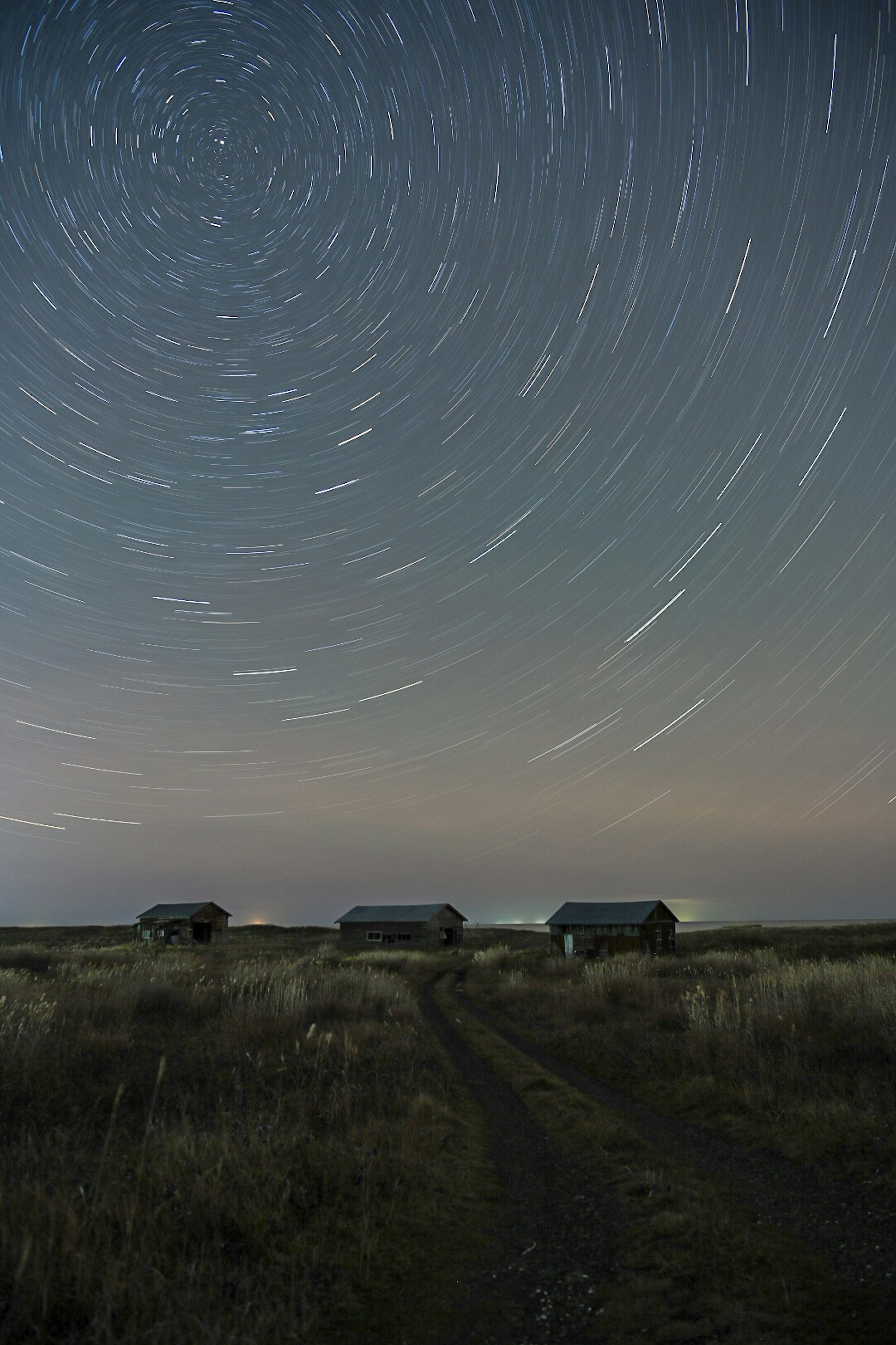 Star trails in the night sky with cabins along a dirt path