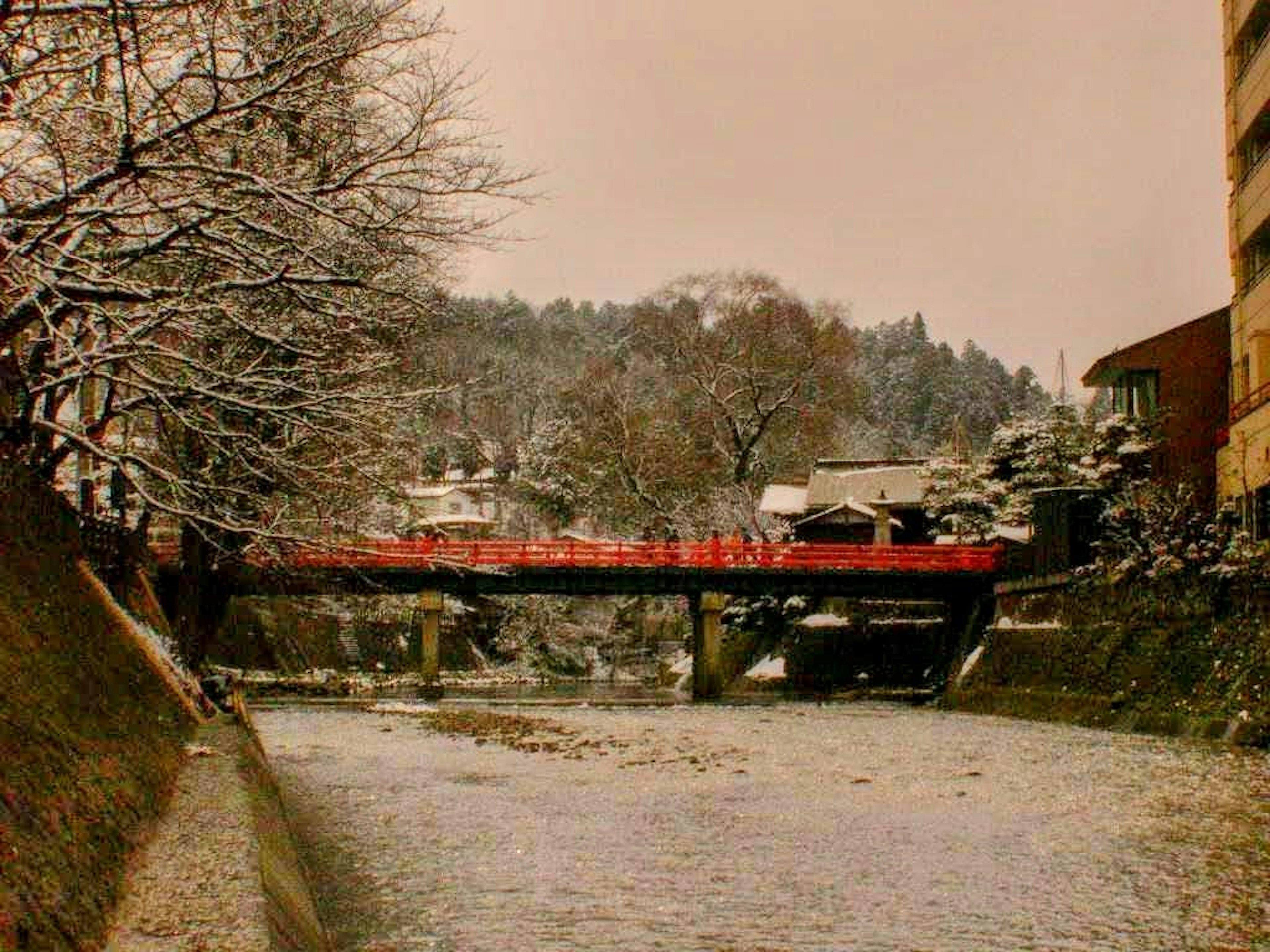 Schneebedeckte Flusslandschaft mit einer roten Brücke