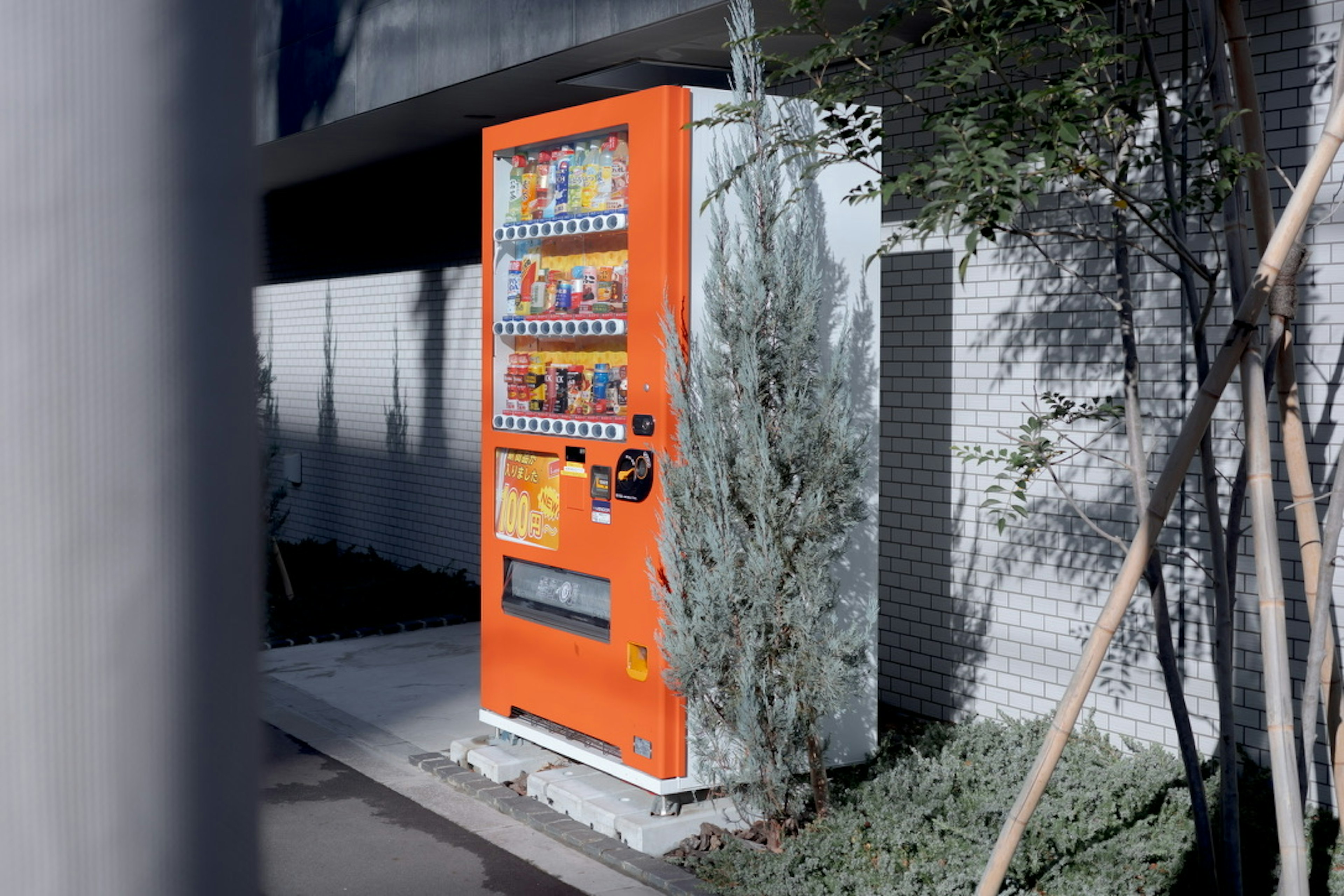 An orange vending machine standing beside greenery