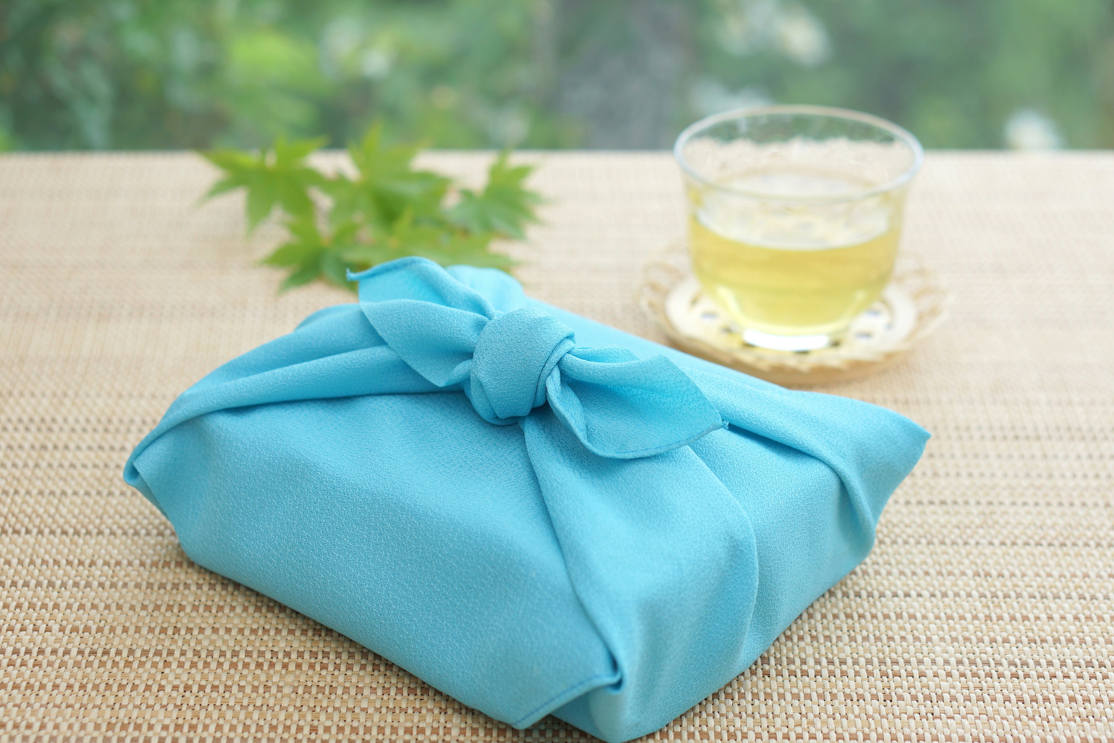 A gift wrapped in blue fabric with a cup of tea in the background