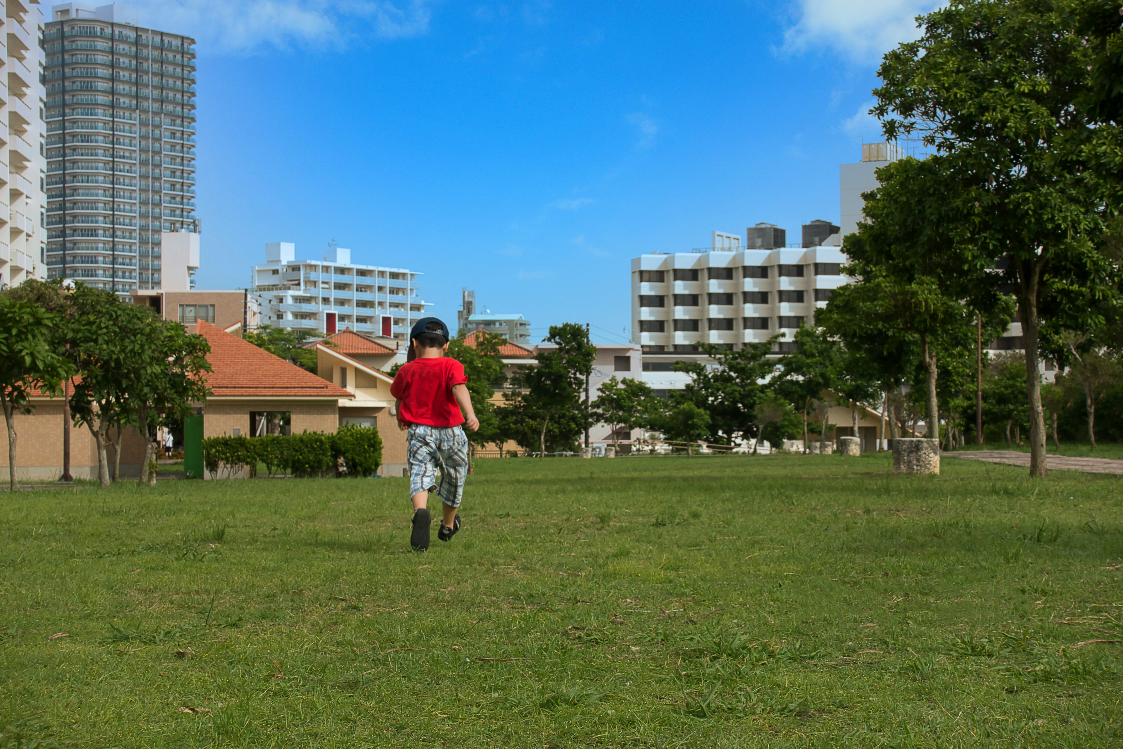 Un homme en chemise rouge marchant dans un parc avec des immeubles et un ciel bleu