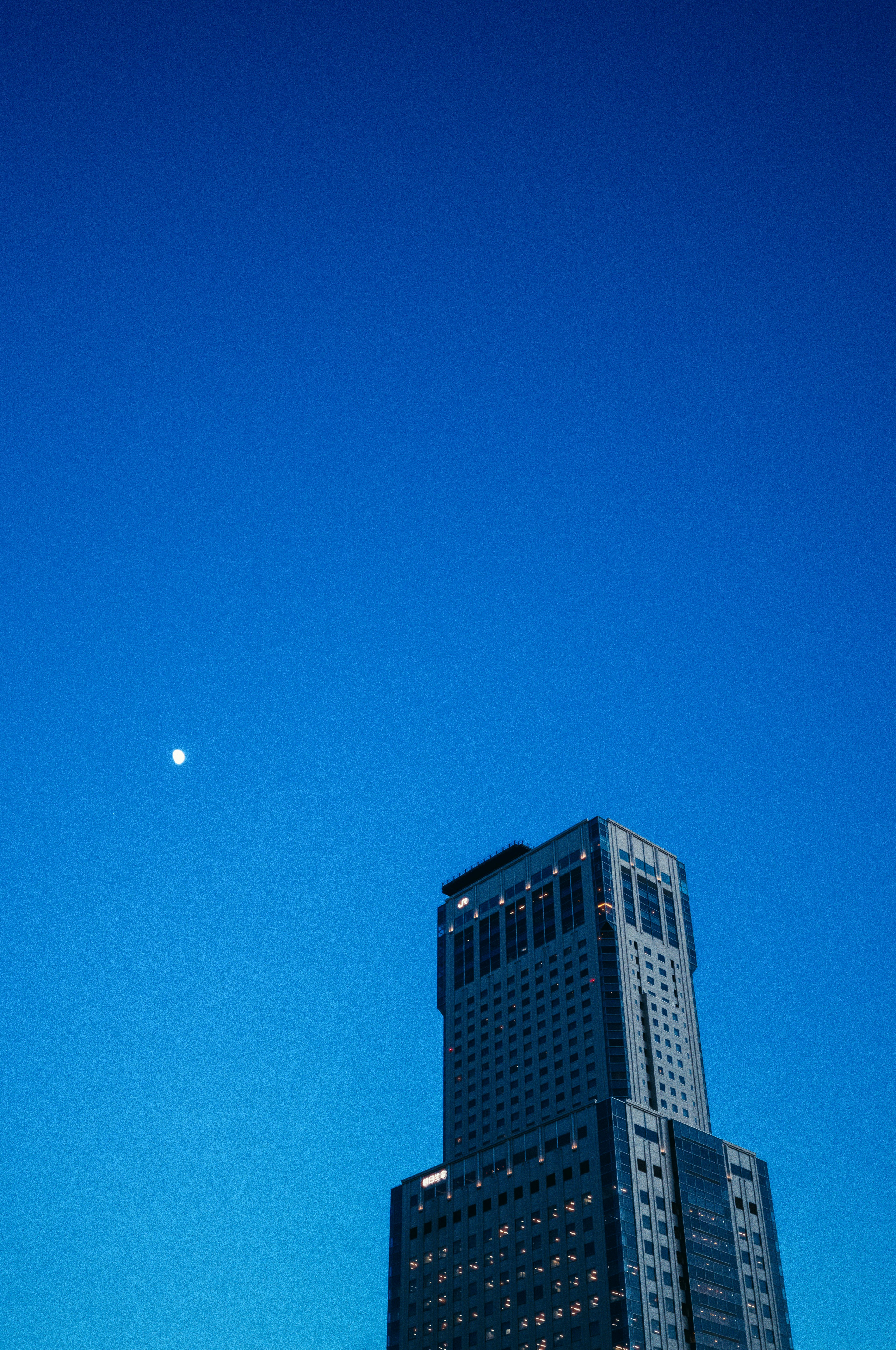 青い空に浮かぶ月と高層ビルの風景