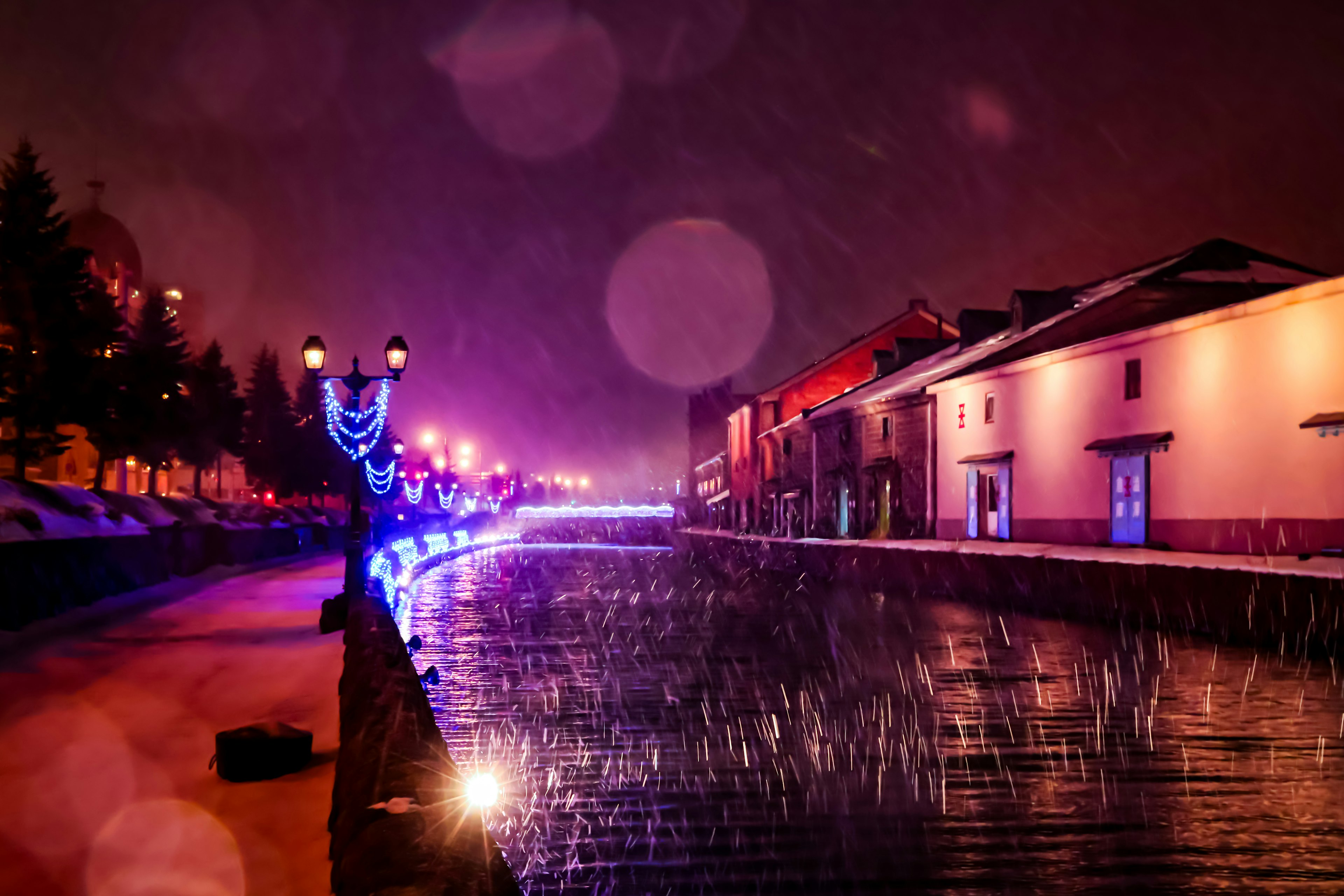 A scenic view of a canal at night illuminated by purple and blue lights