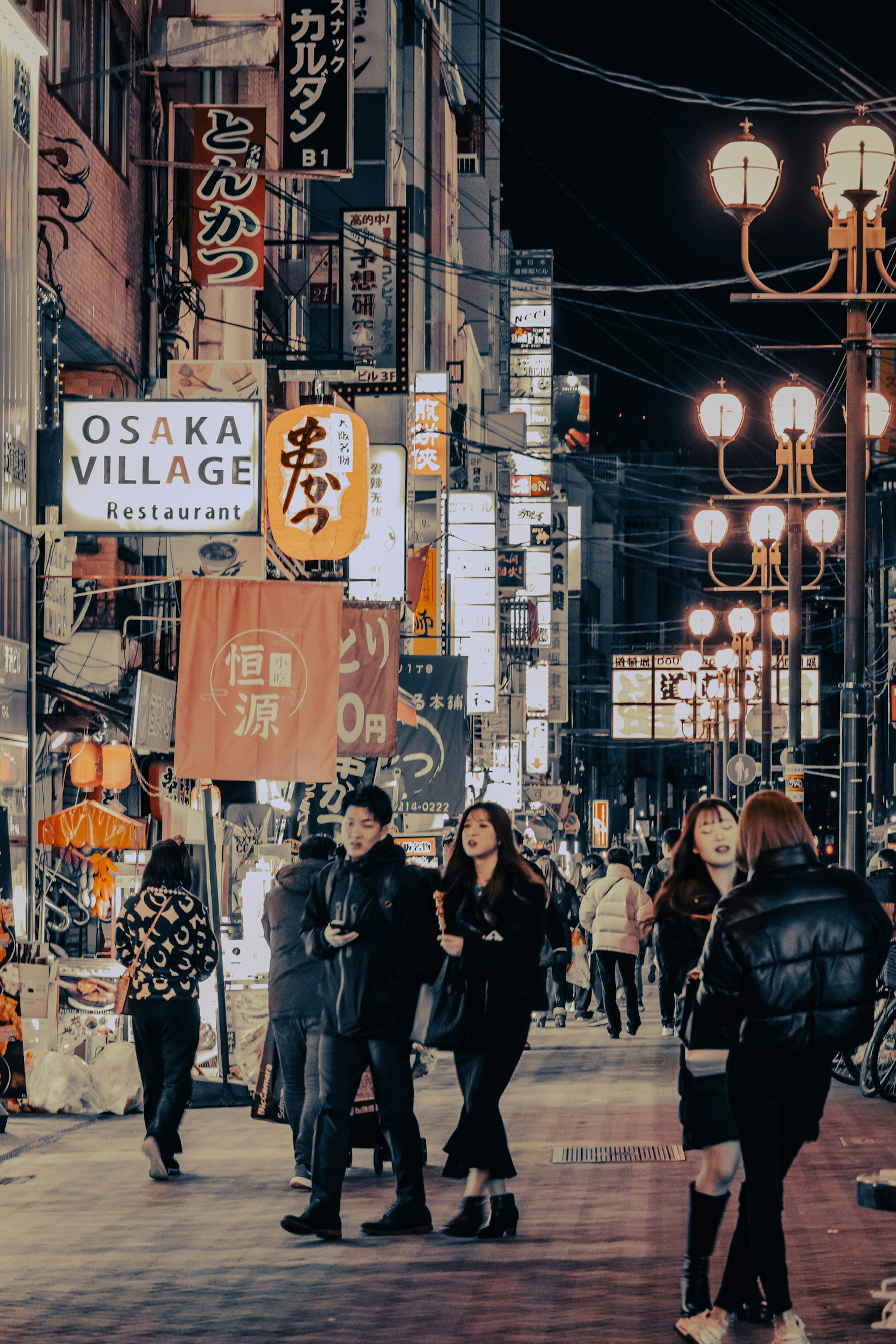 Strada affollata di Osaka con persone e numerosi cartelli di notte