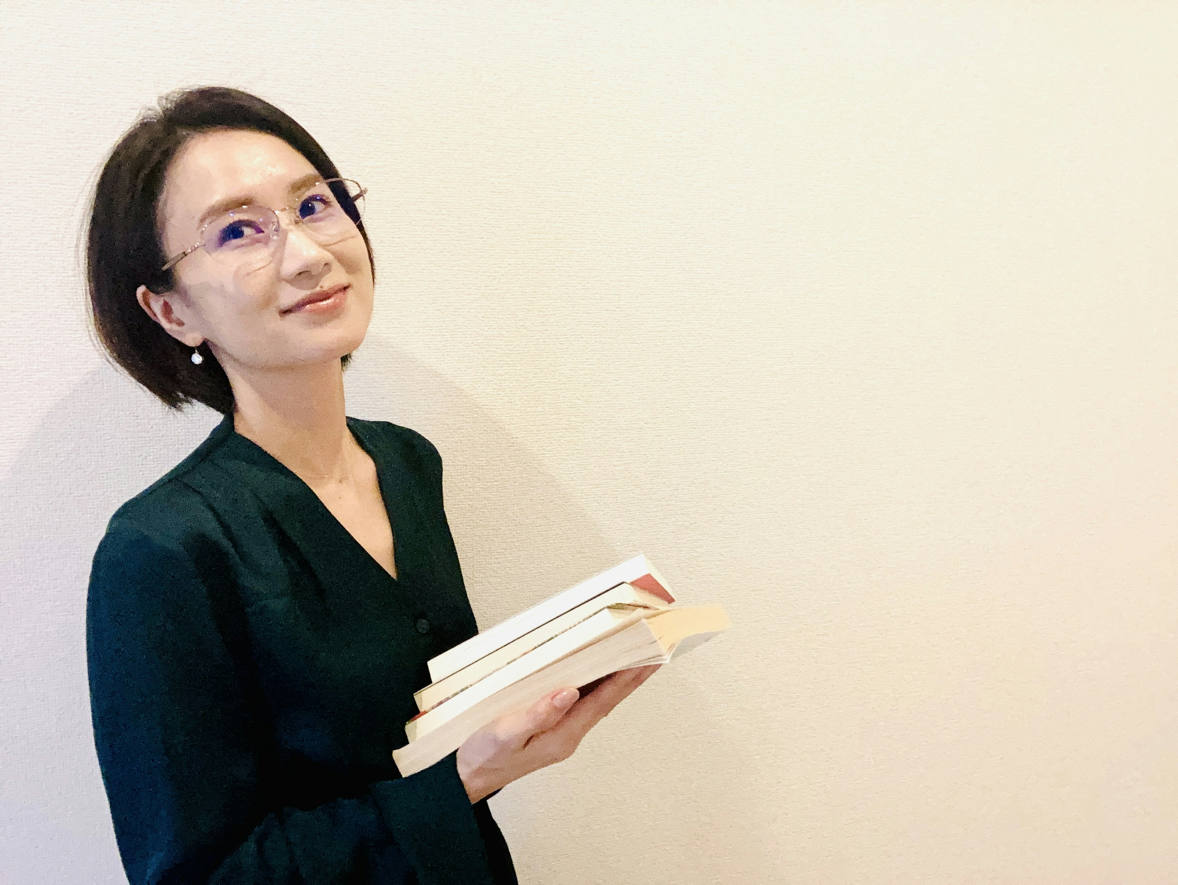 A woman holding books with a smile against a simple background