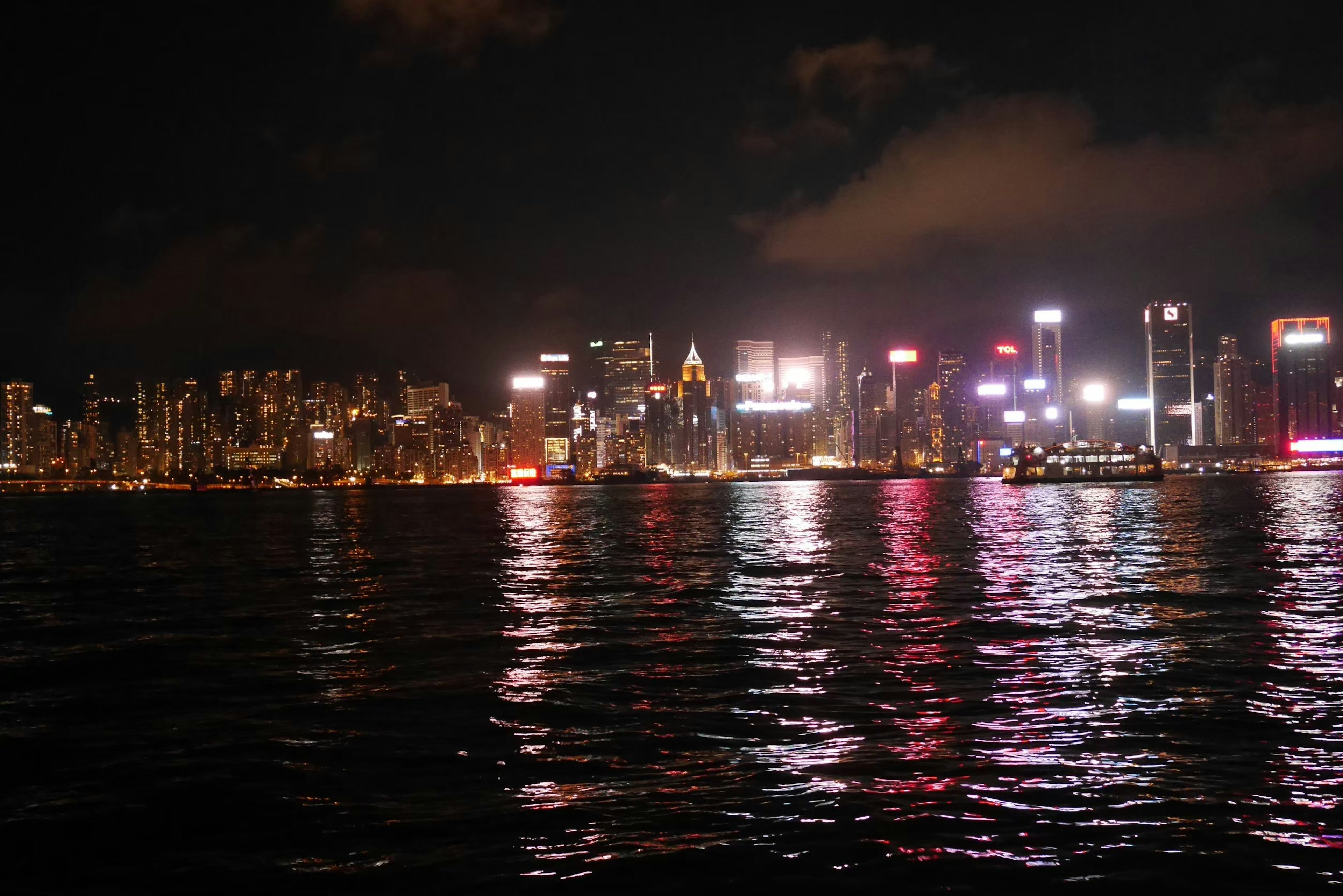 Pemandangan malam garis langit Hong Kong dengan gedung pencakar langit yang diterangi yang memantul di atas air