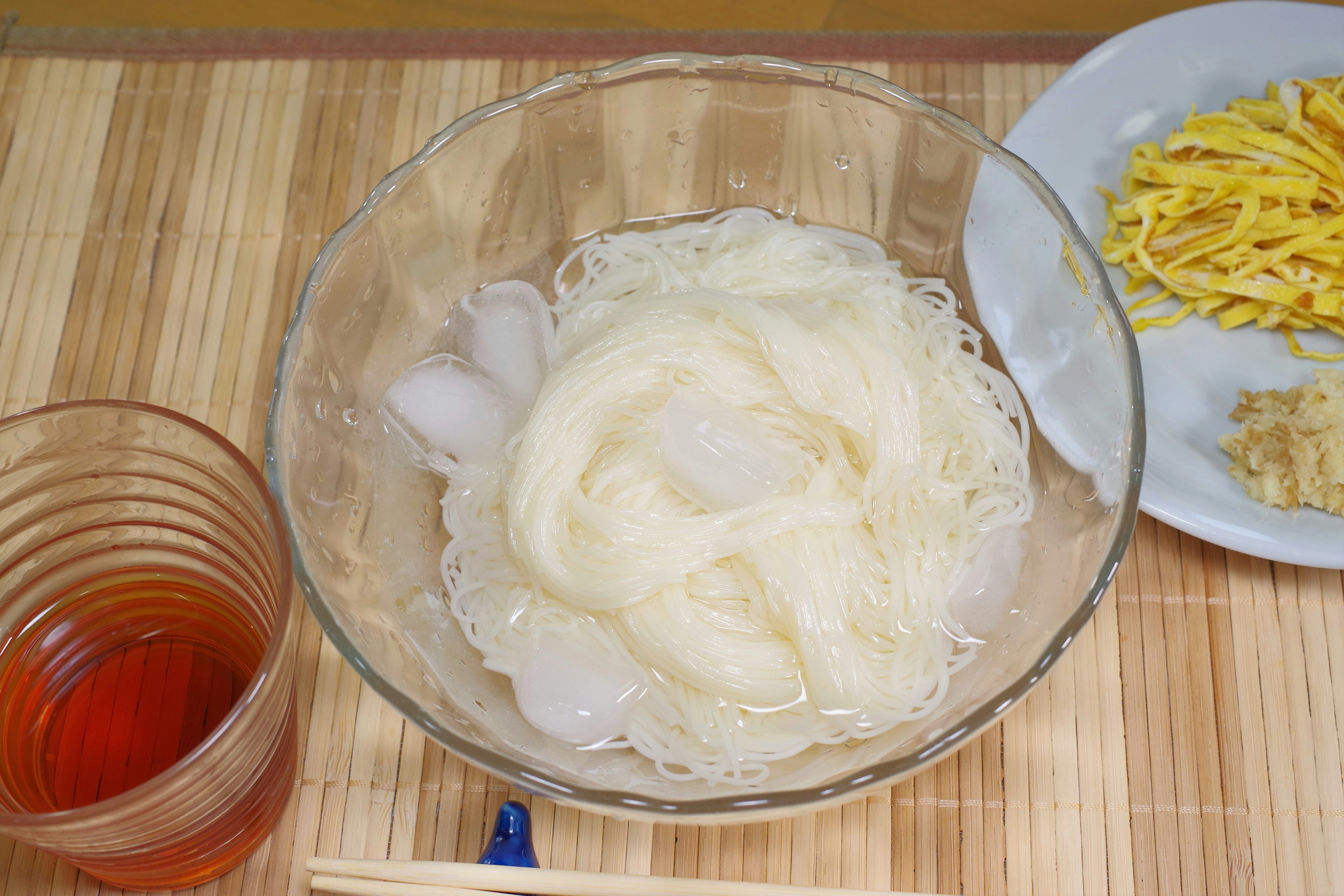 Mie dingin dalam mangkuk dengan es dan piring samping telur dan jahe