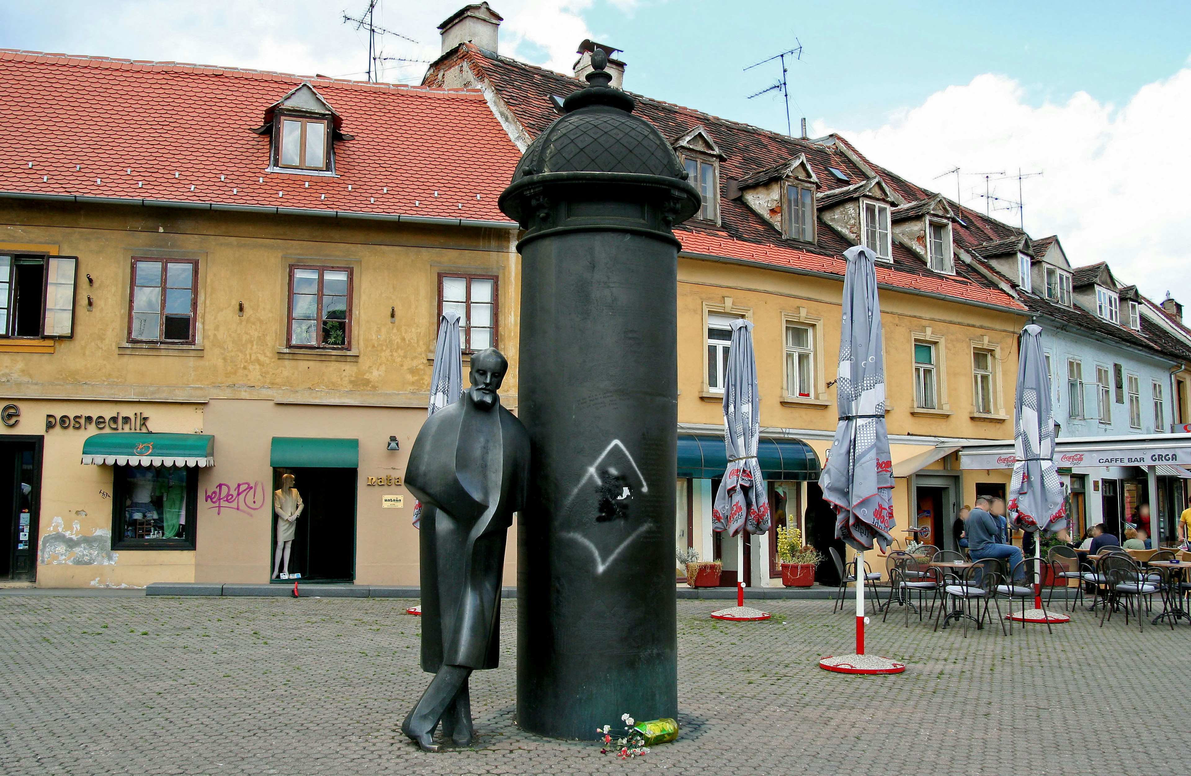 Skulptur eines Mannes, der sich an einer großen Säule in einem Stadtplatz lehnt