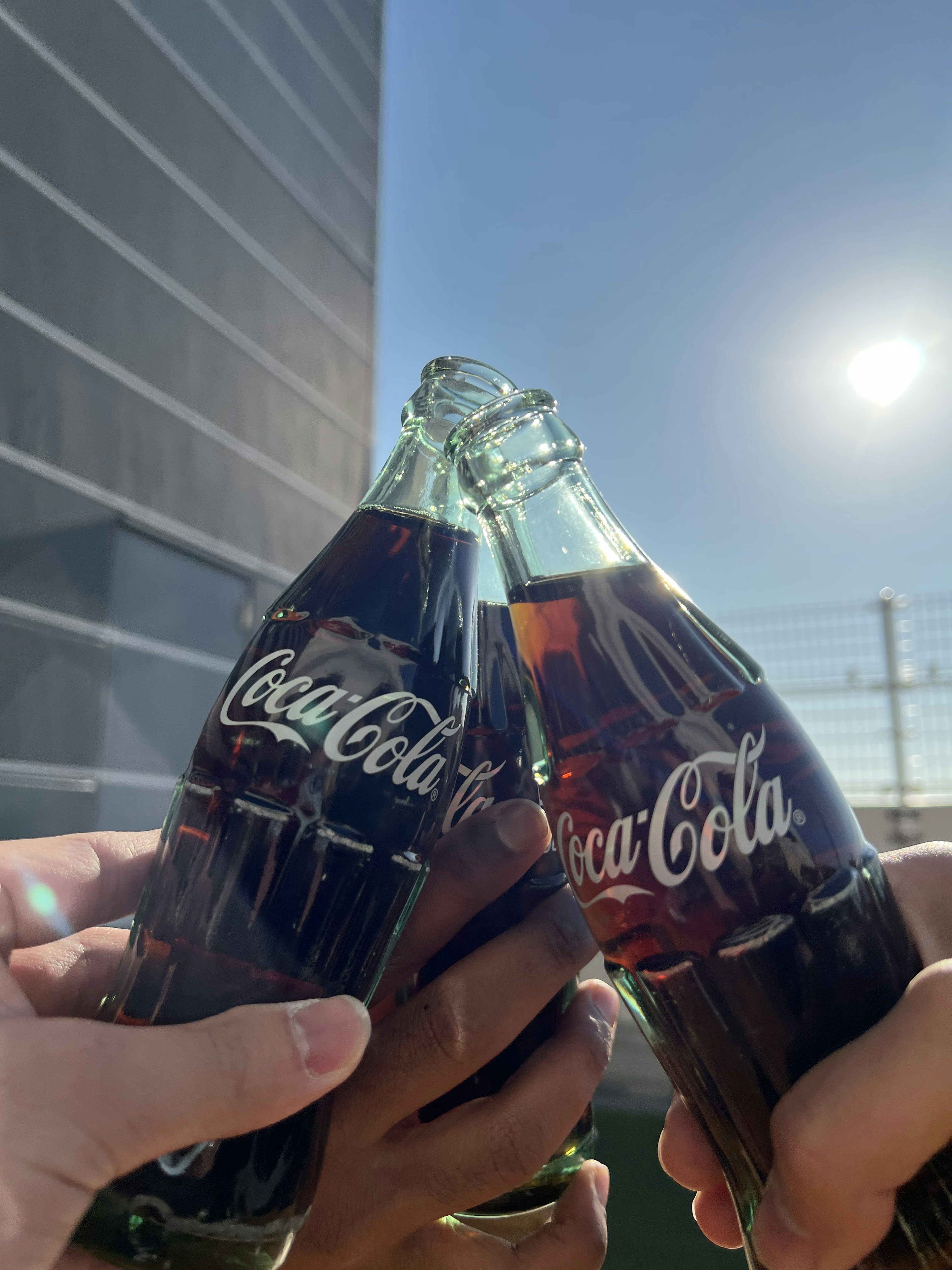 Mani che brindano con bottiglie di Coca-Cola sotto un cielo blu