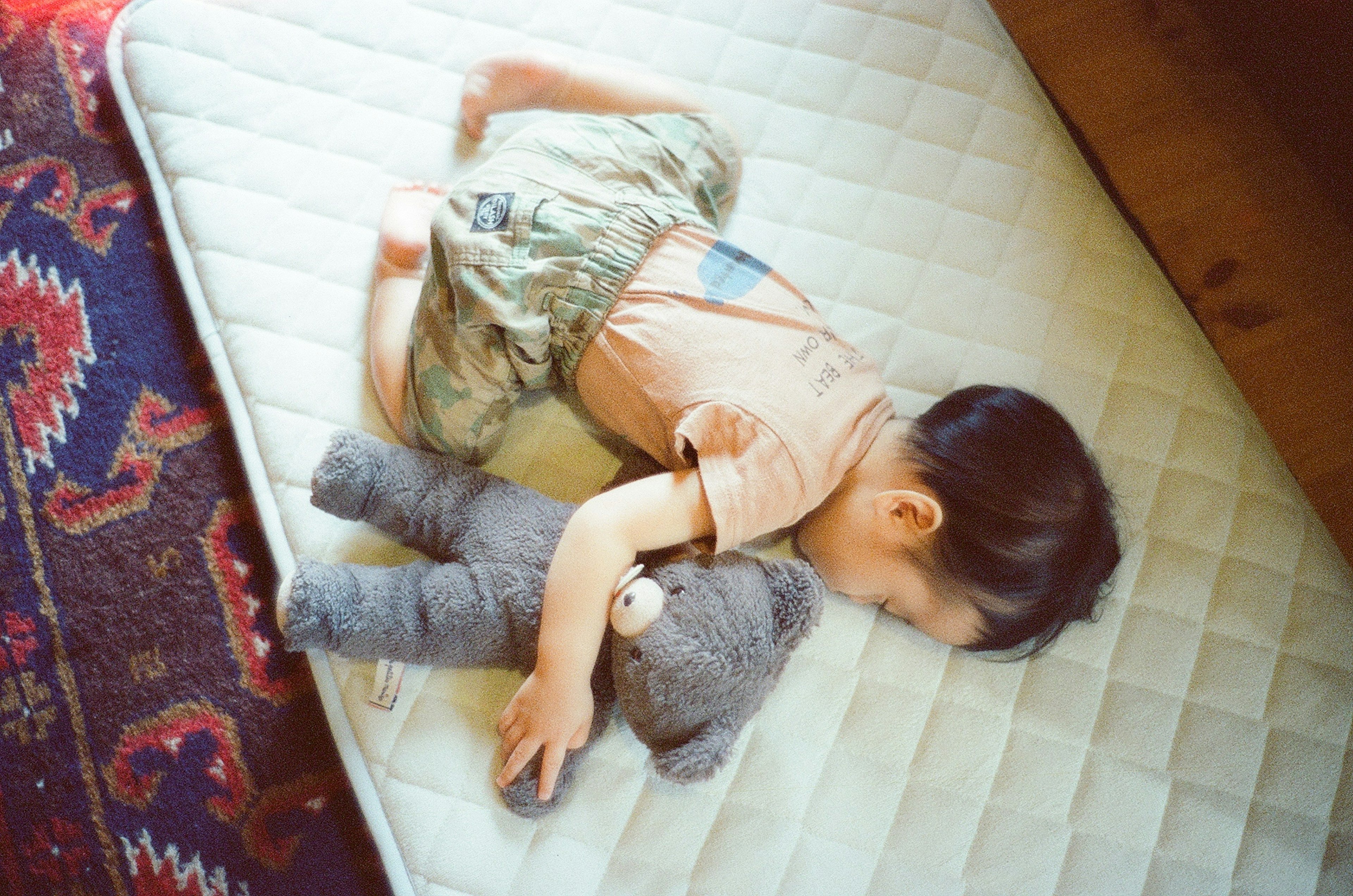 Un bebé durmiendo con un oso de peluche gris sobre un colchón blanco