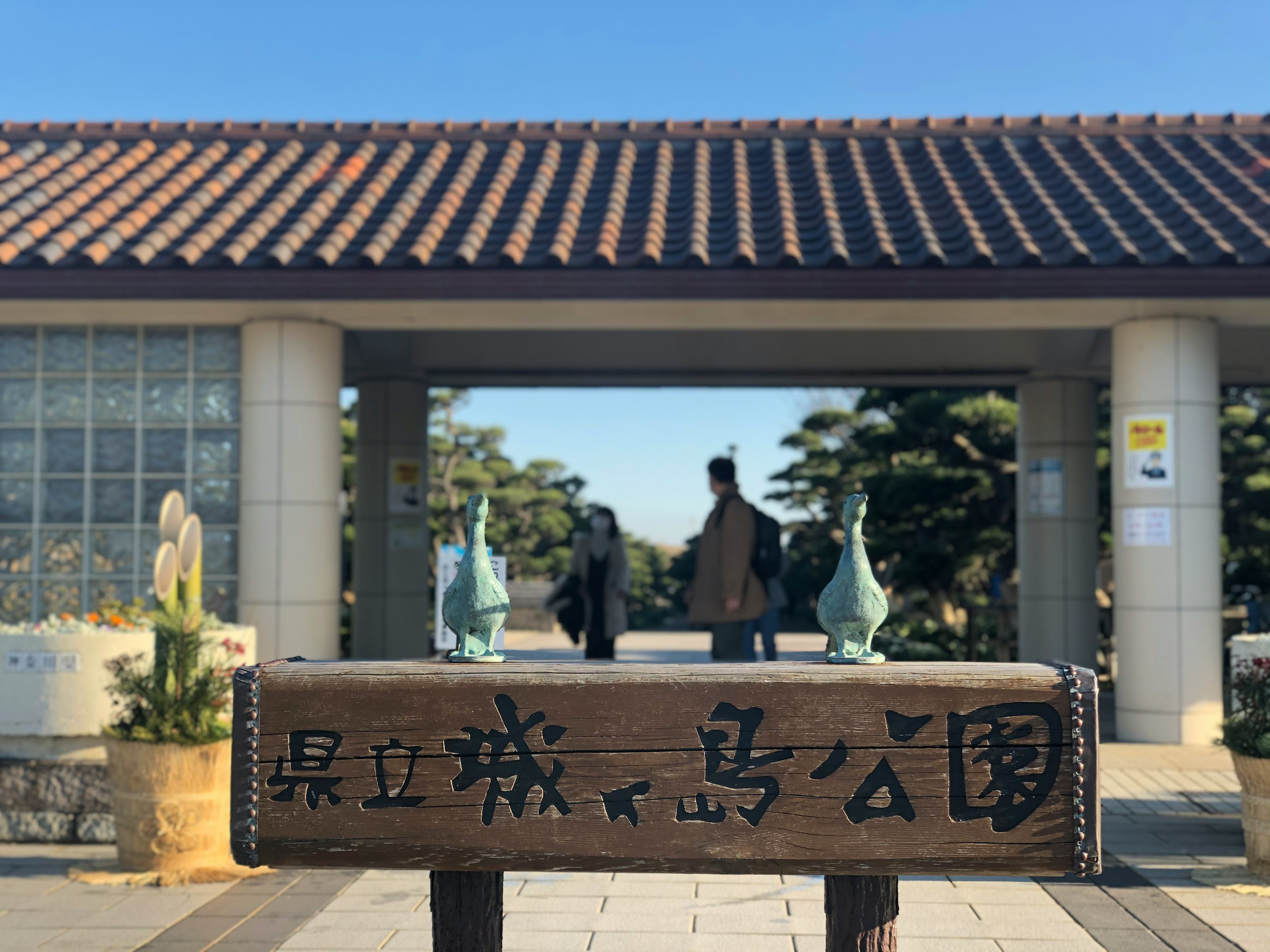 門の前にある木製の看板に書かれた公園の名前と背景に見える人々