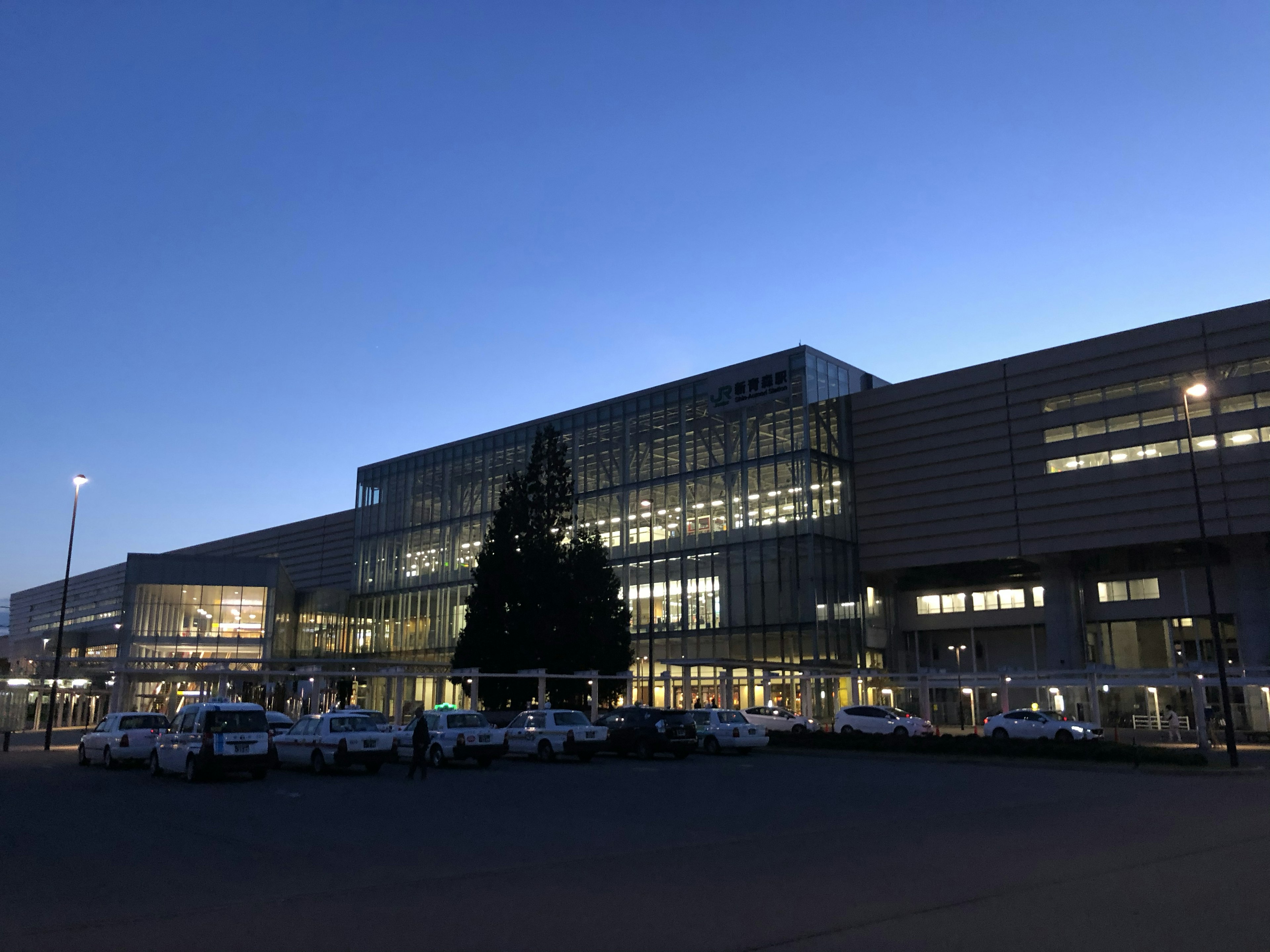 Edificio moderno del aeropuerto al anochecer con fachada iluminada y vehículos estacionados