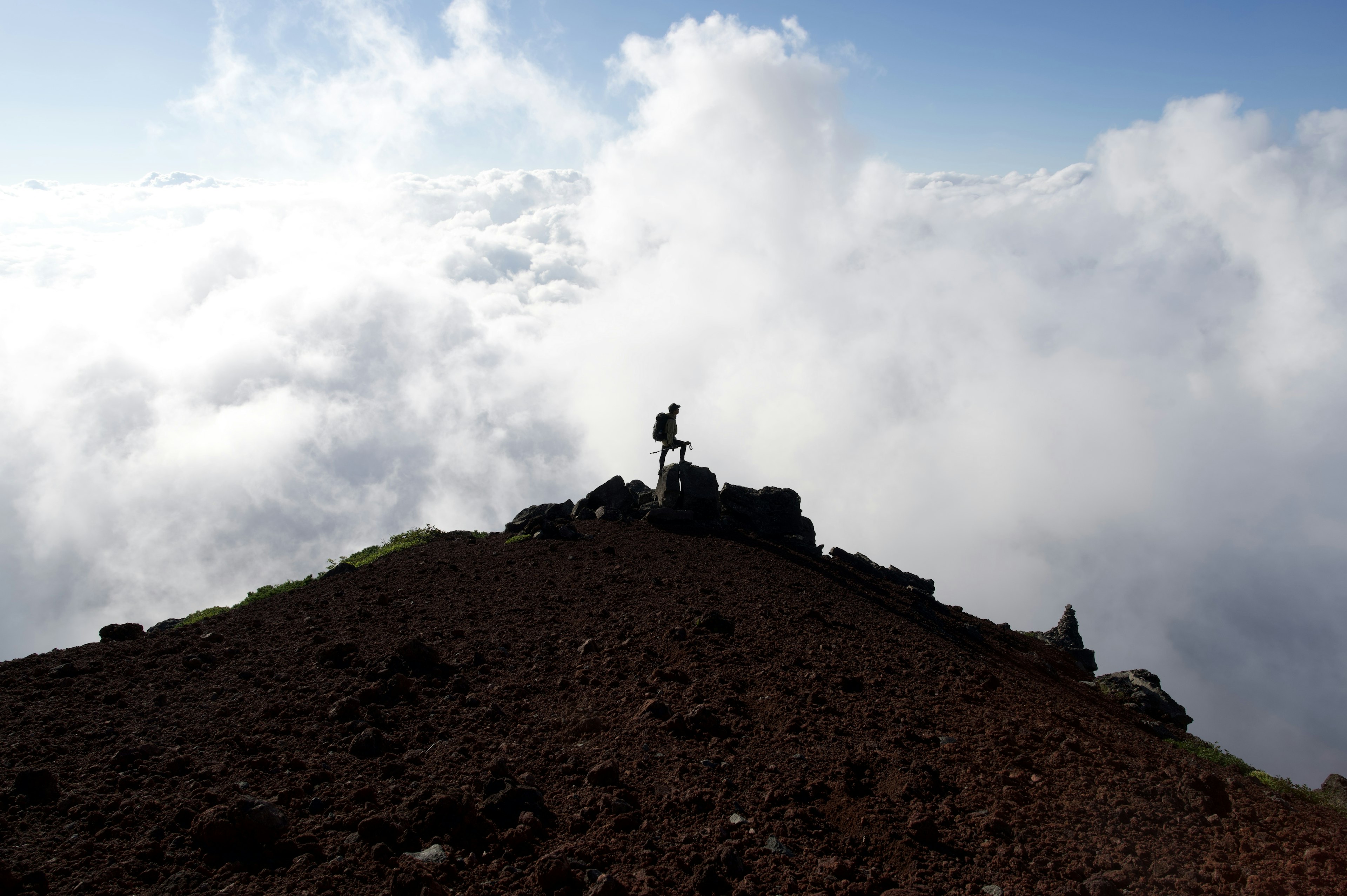 Silueta de un excursionista de pie sobre las nubes en una cima volcánica