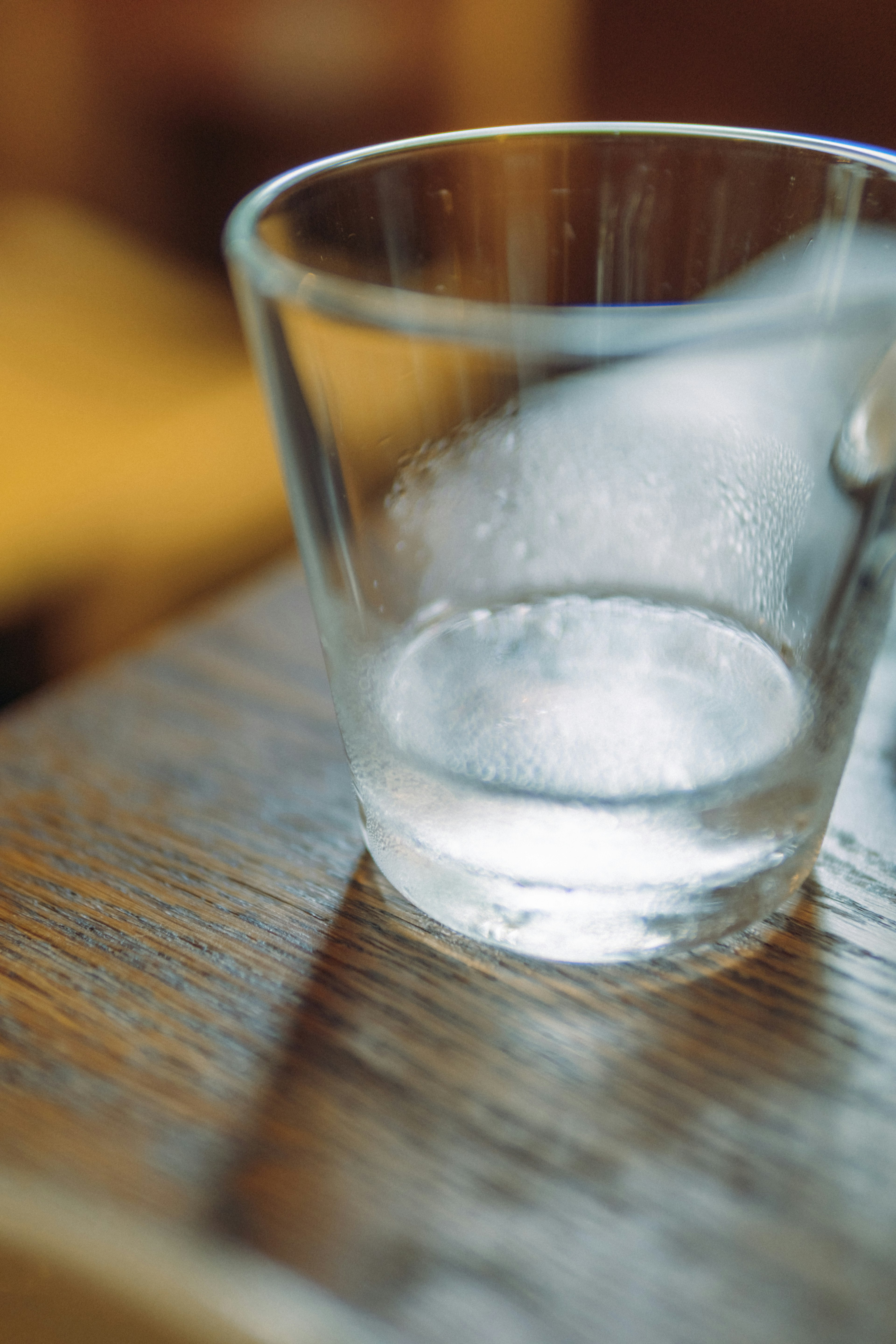 A transparent glass sits on a wooden table